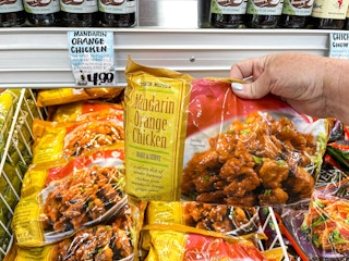 A person's hand holding a bag of Trader Ming's Mandarin Orange Chicken above a display of them at Trader Joe's.
