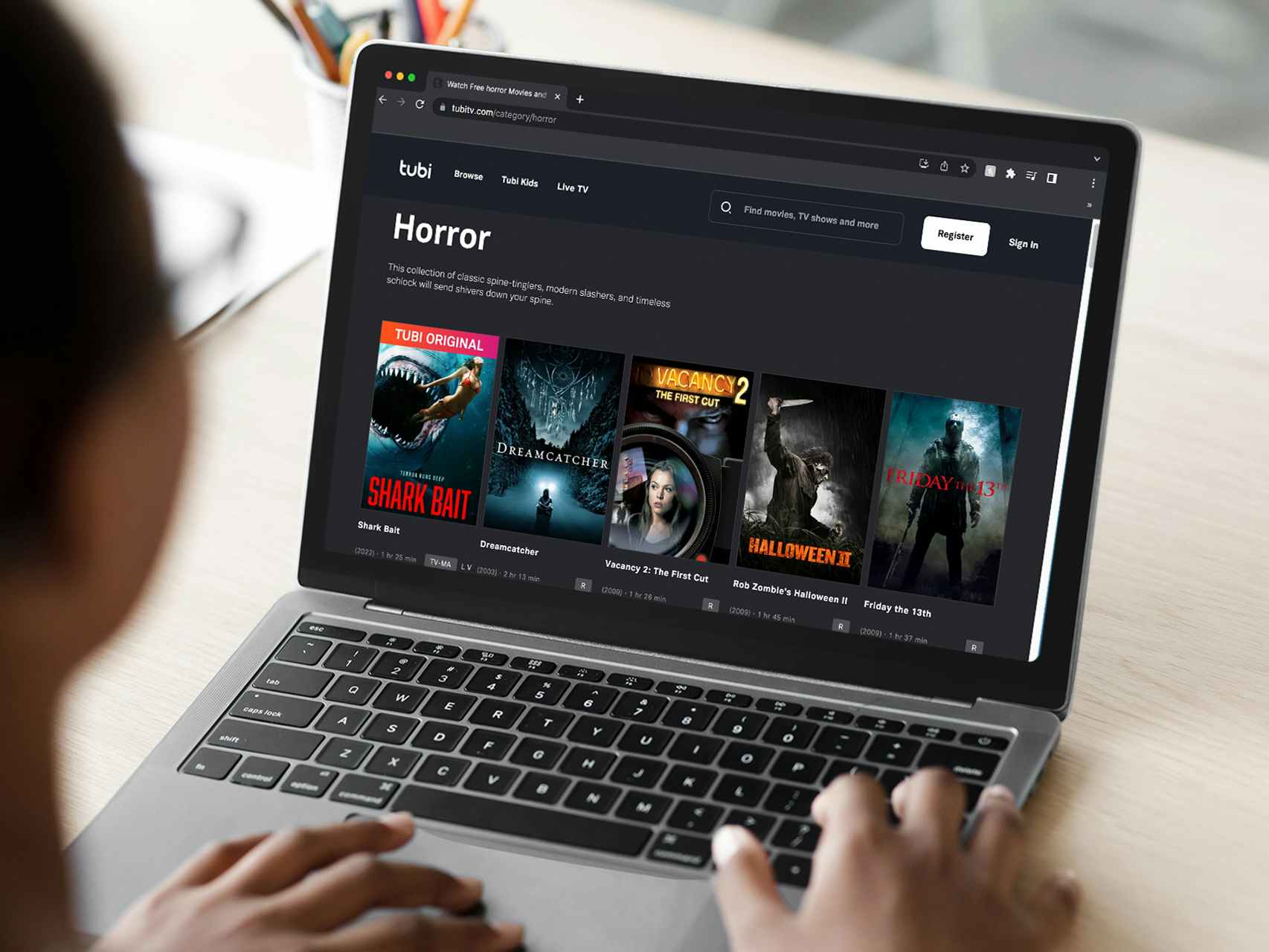 A person using a laptop to browse the Horror movie selection on the Tubi website.