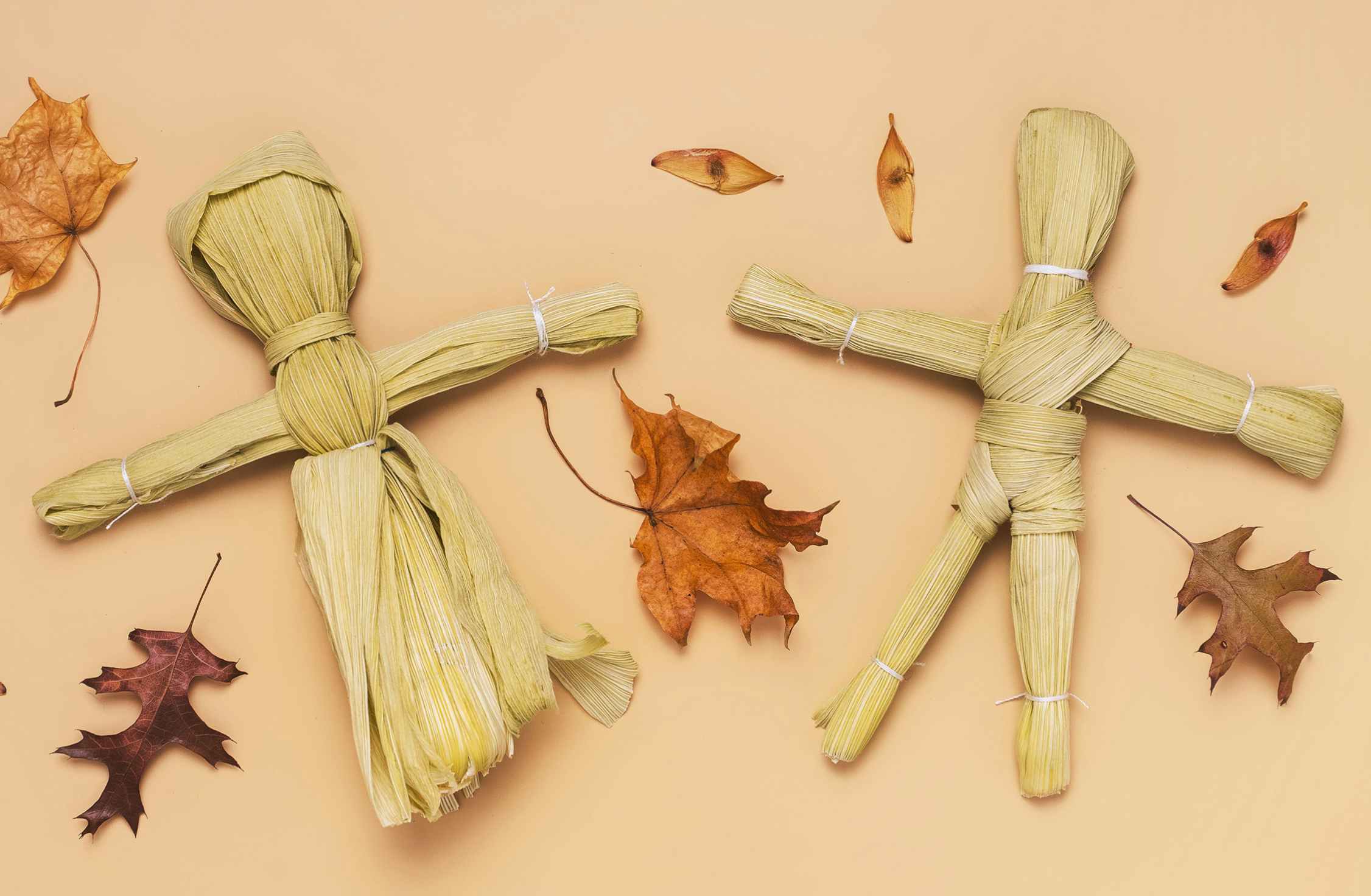 two DIY corn husk dolls with scattered leaves