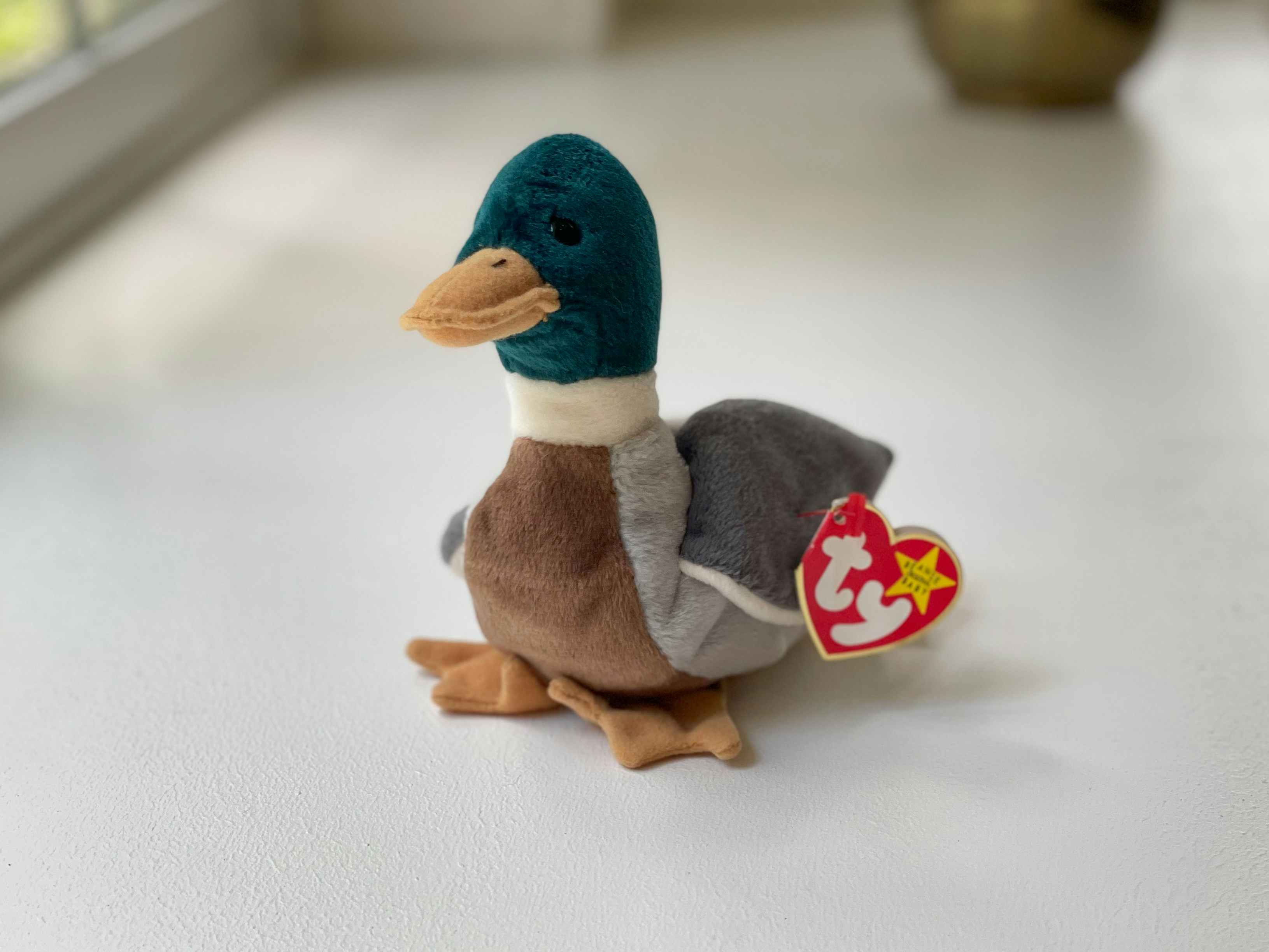 A Jake the Duck beanie baby sitting on a white table.