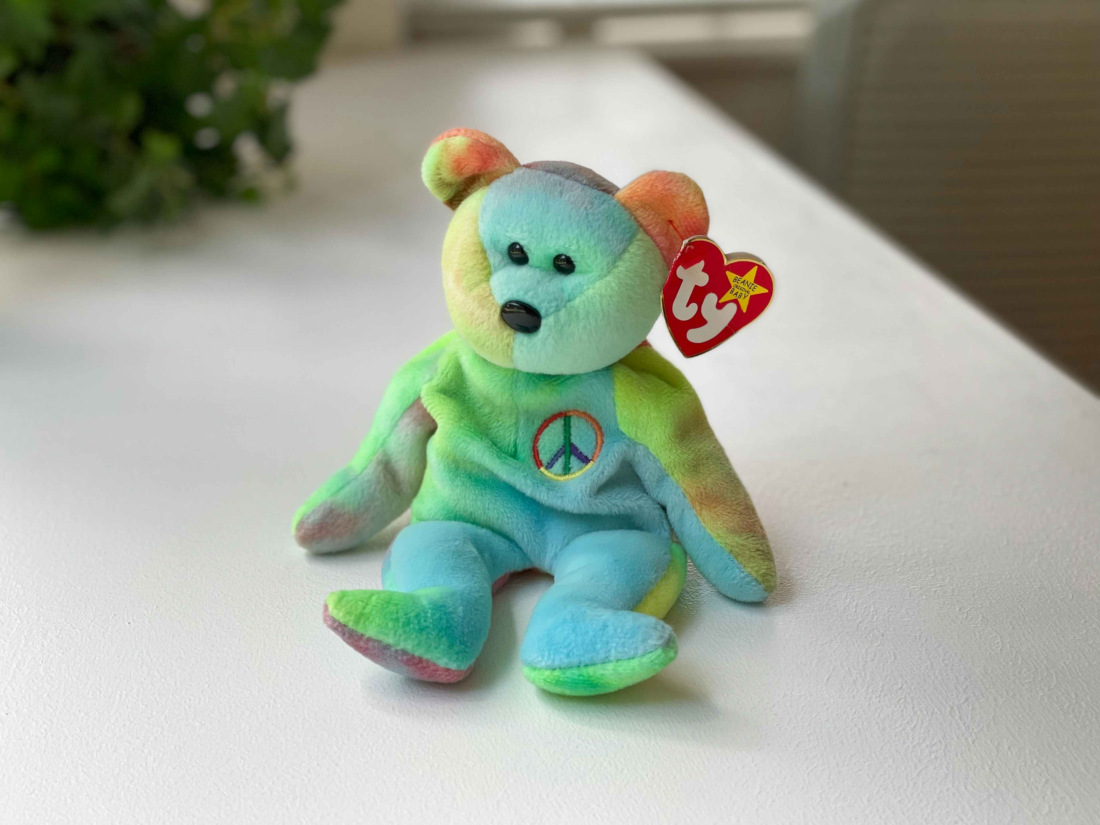 A Peace the Bear beanie baby sitting on a white table.