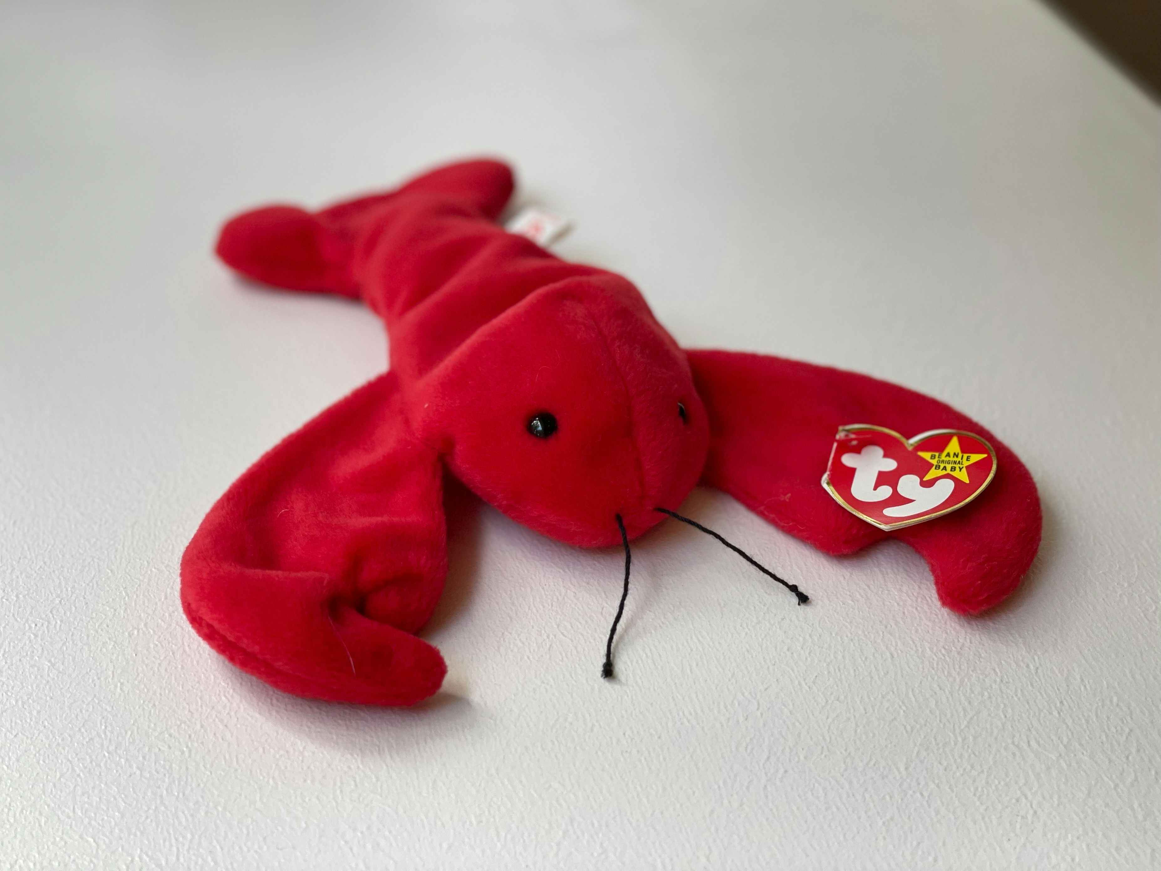 A Pinchers the Lobster beanie baby sitting on a white table.