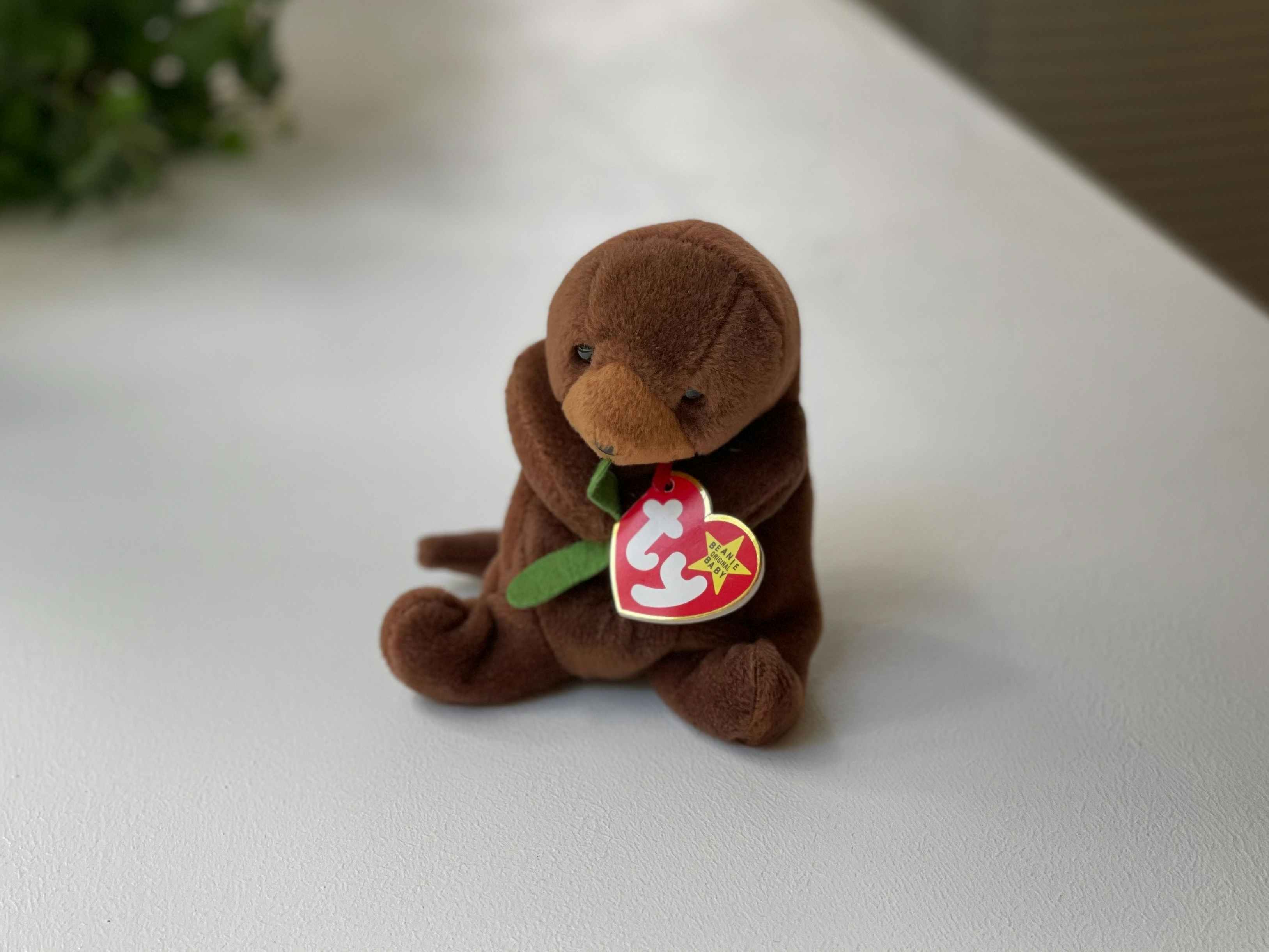 A Seaweed the Otter beanie baby sitting on a white table.