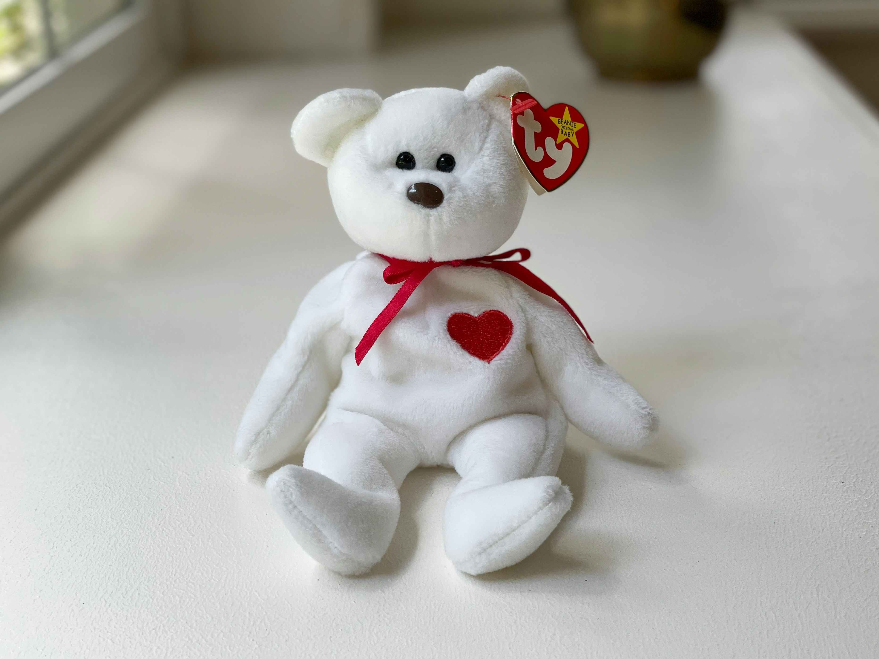 A Valentino the Bear beanie baby sitting on a white table.
