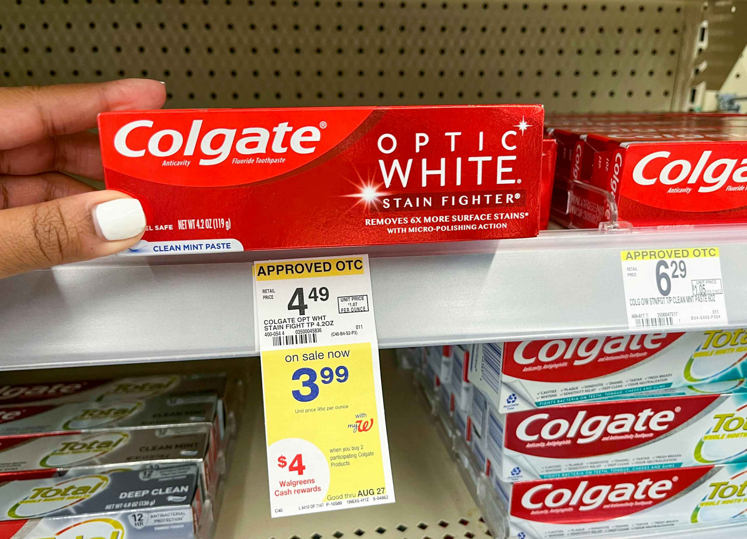 hand touching box of colgate Optic White stainfighter toothpaste on shelf with sales tag underneath