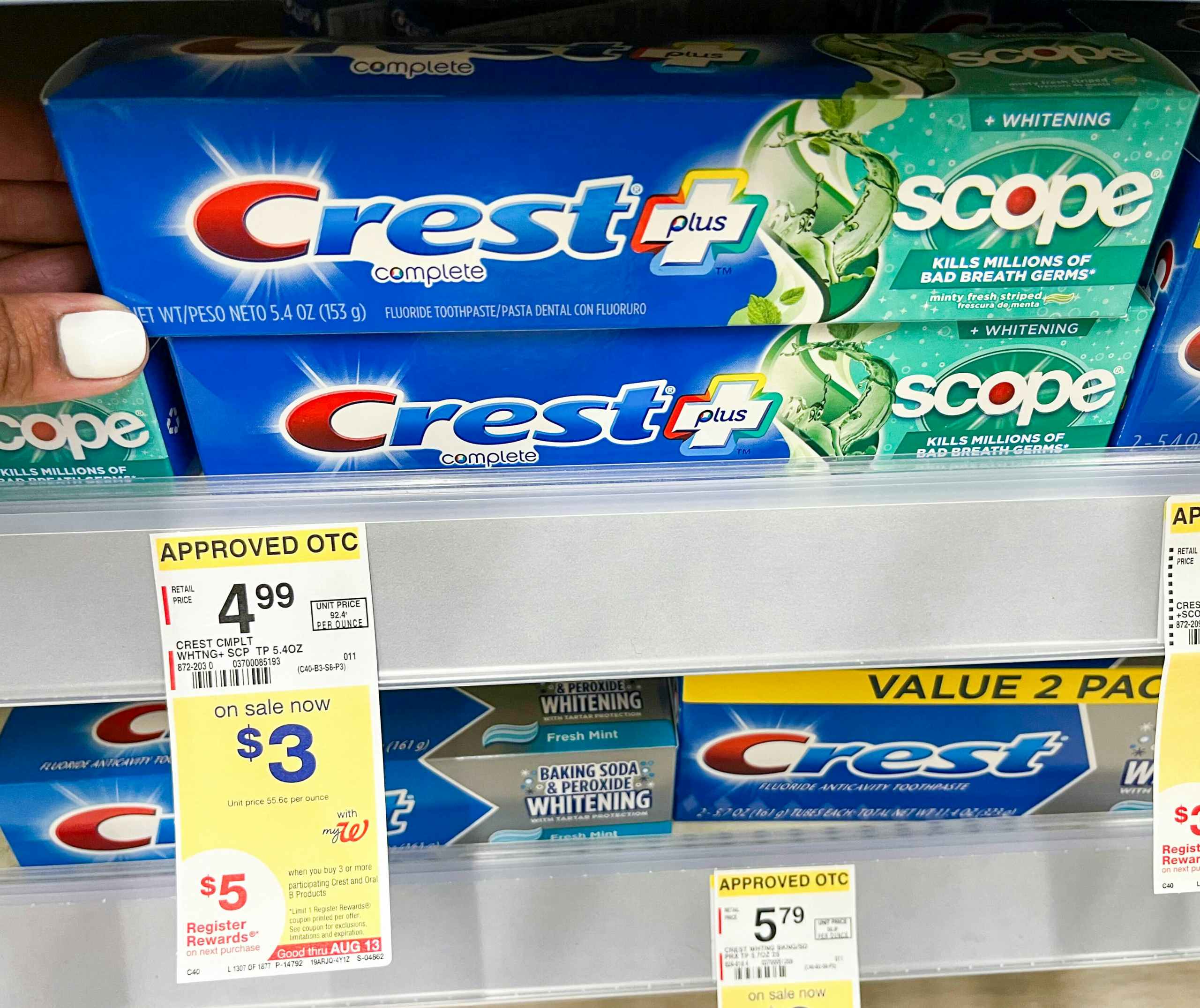 hand touching box of Crest plus Scope toothpaste with price tag underneath