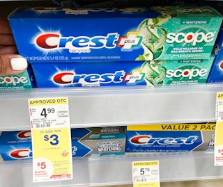 hand touching box of Crest plus Scope toothpaste with price tag underneath