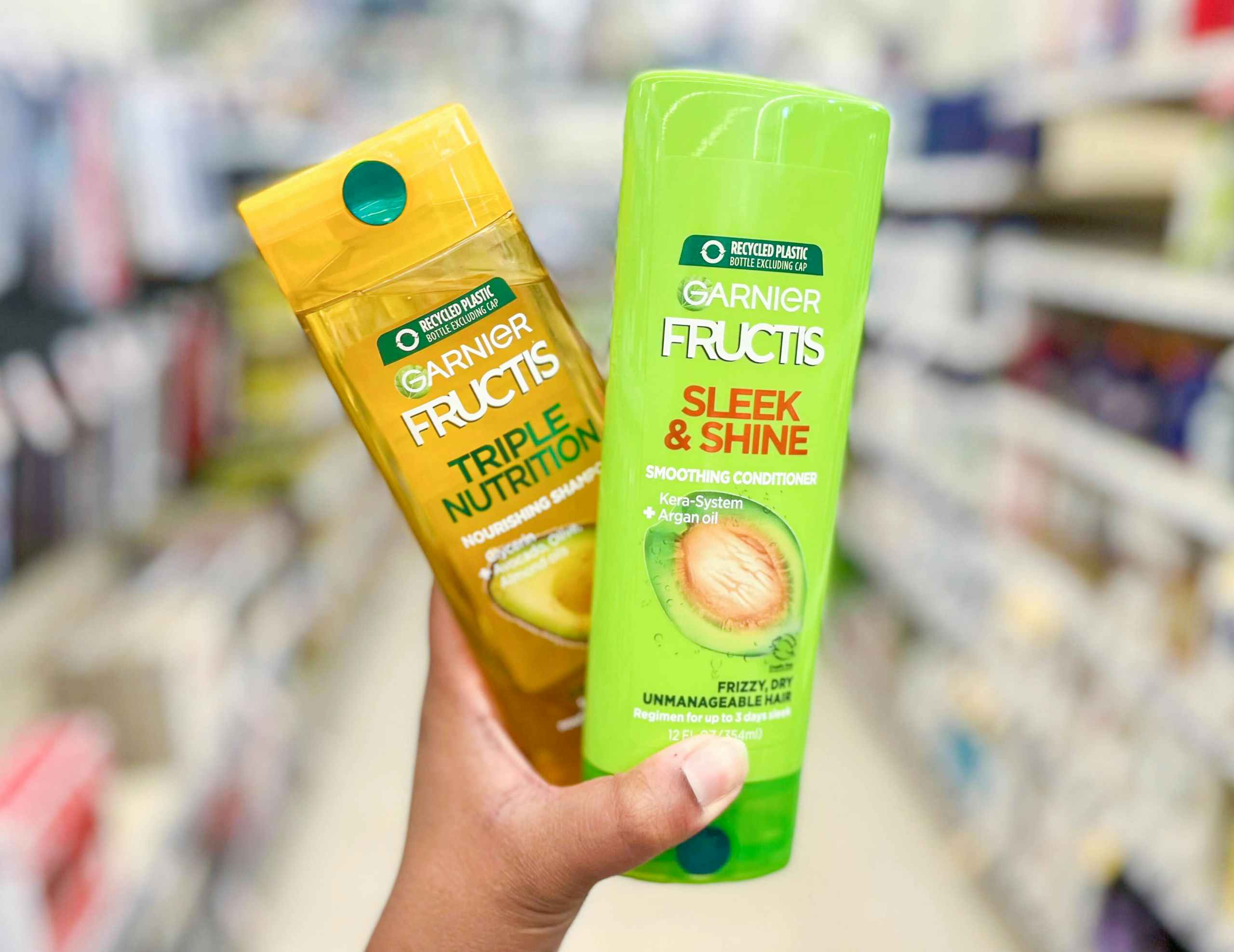 hand holding two bottles of Garnier Fructis shampoo & conditioner in aisle