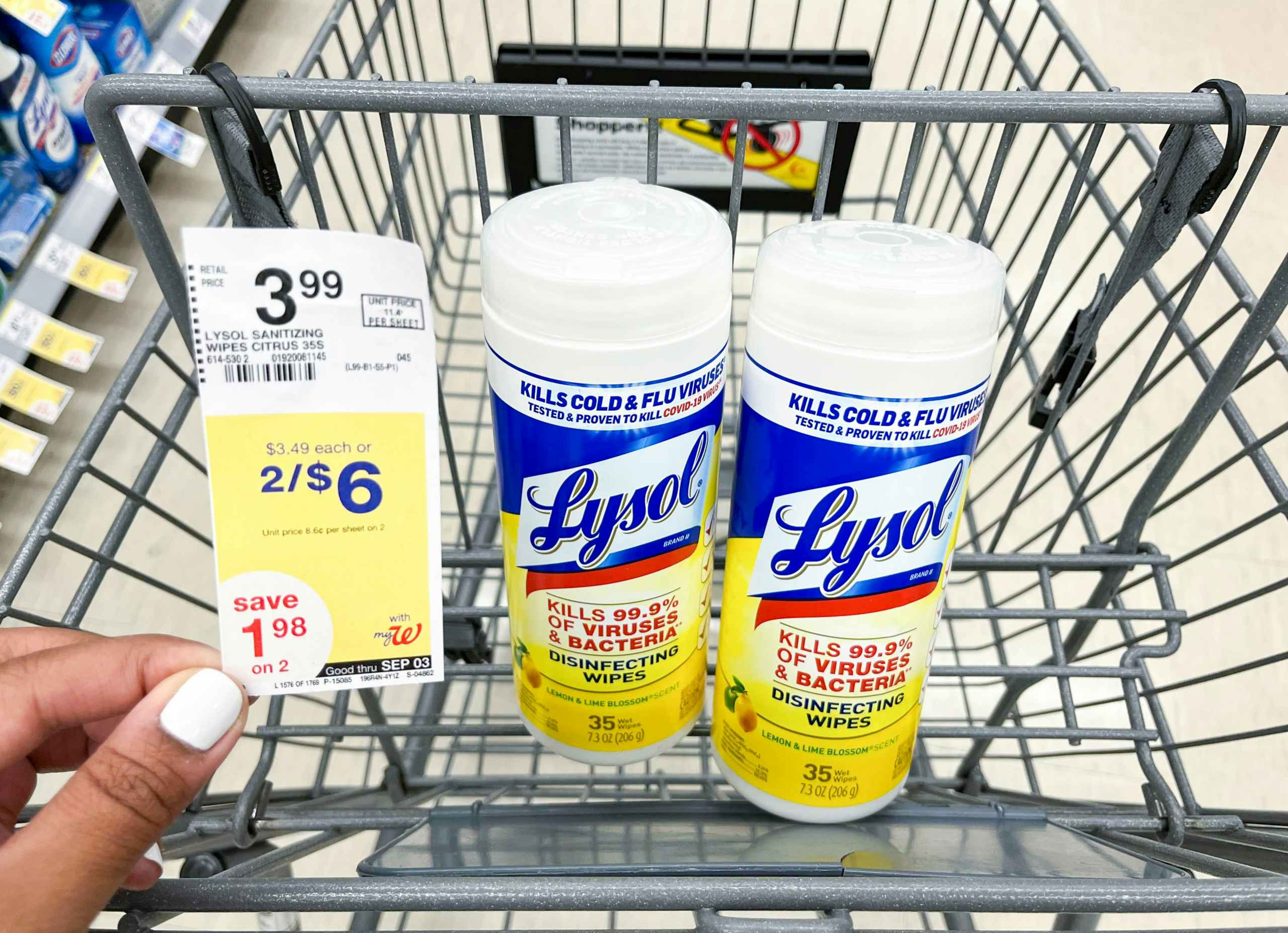 hand holding sales tag next to two containers of Lysol disinfecting wipes inside of shopping cart