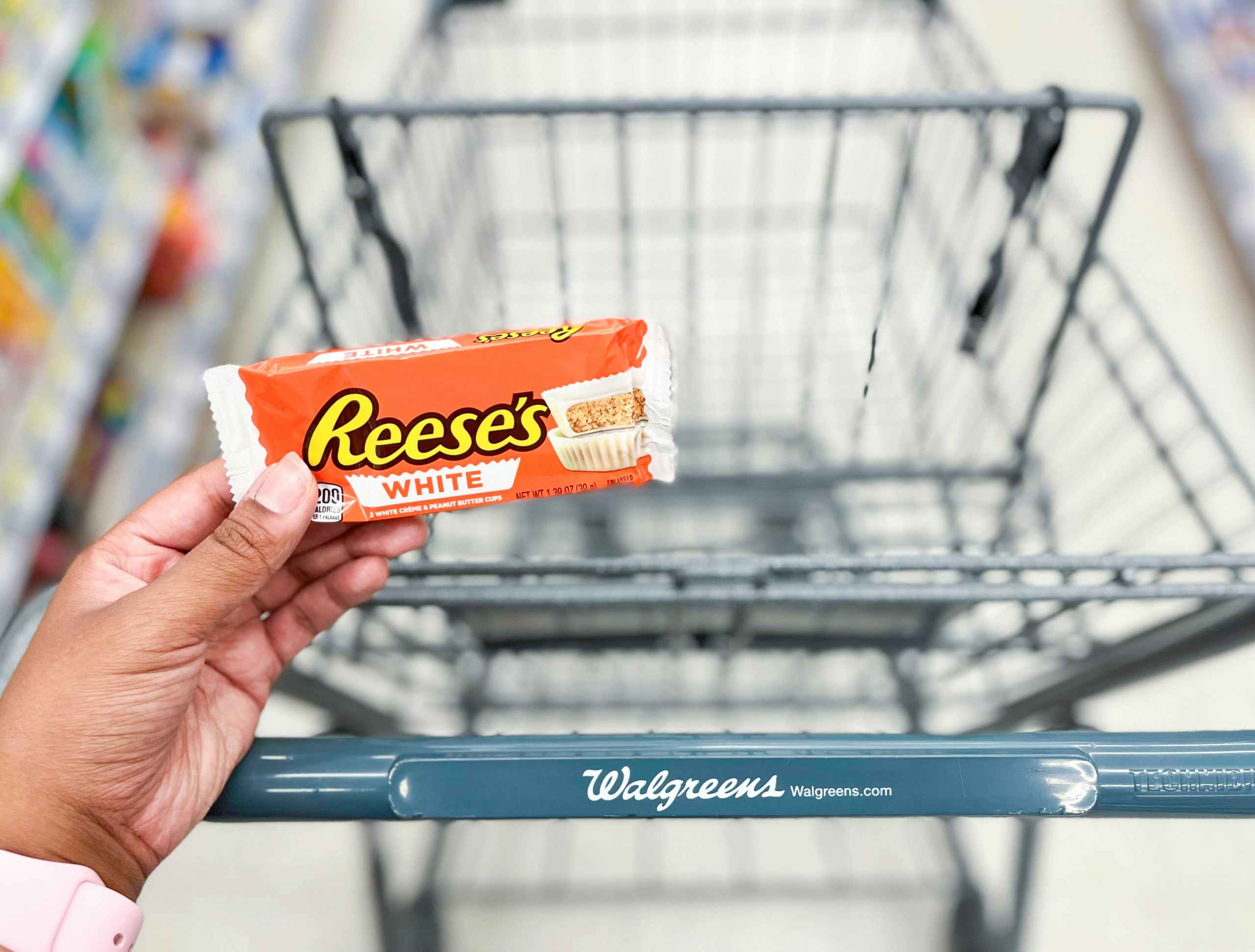 hand holding a pack of Reese's peanut butter cups in front of shopping cart