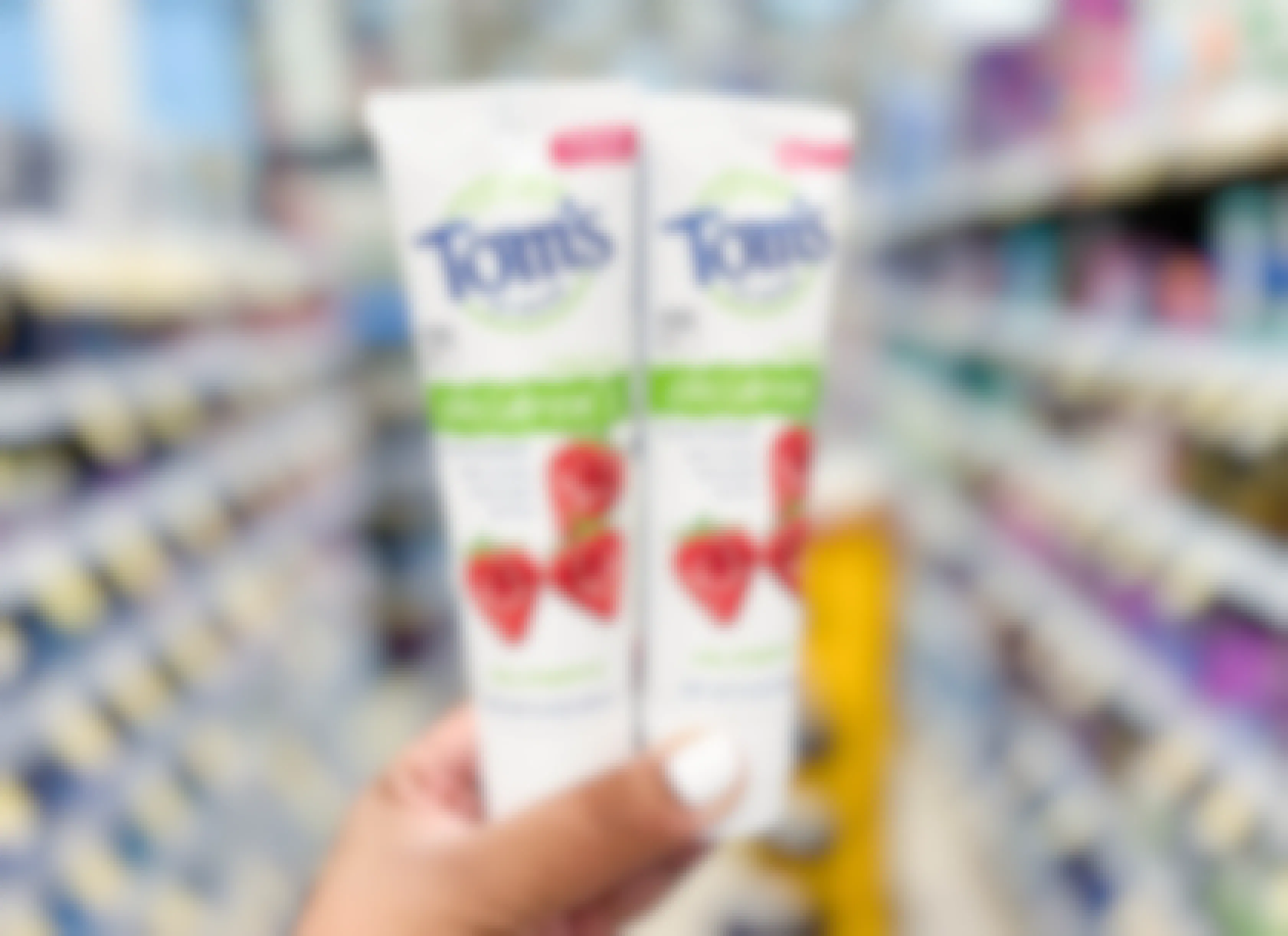 hand holding two tubes of Tom's of Maine Children's toothpaste in aisle