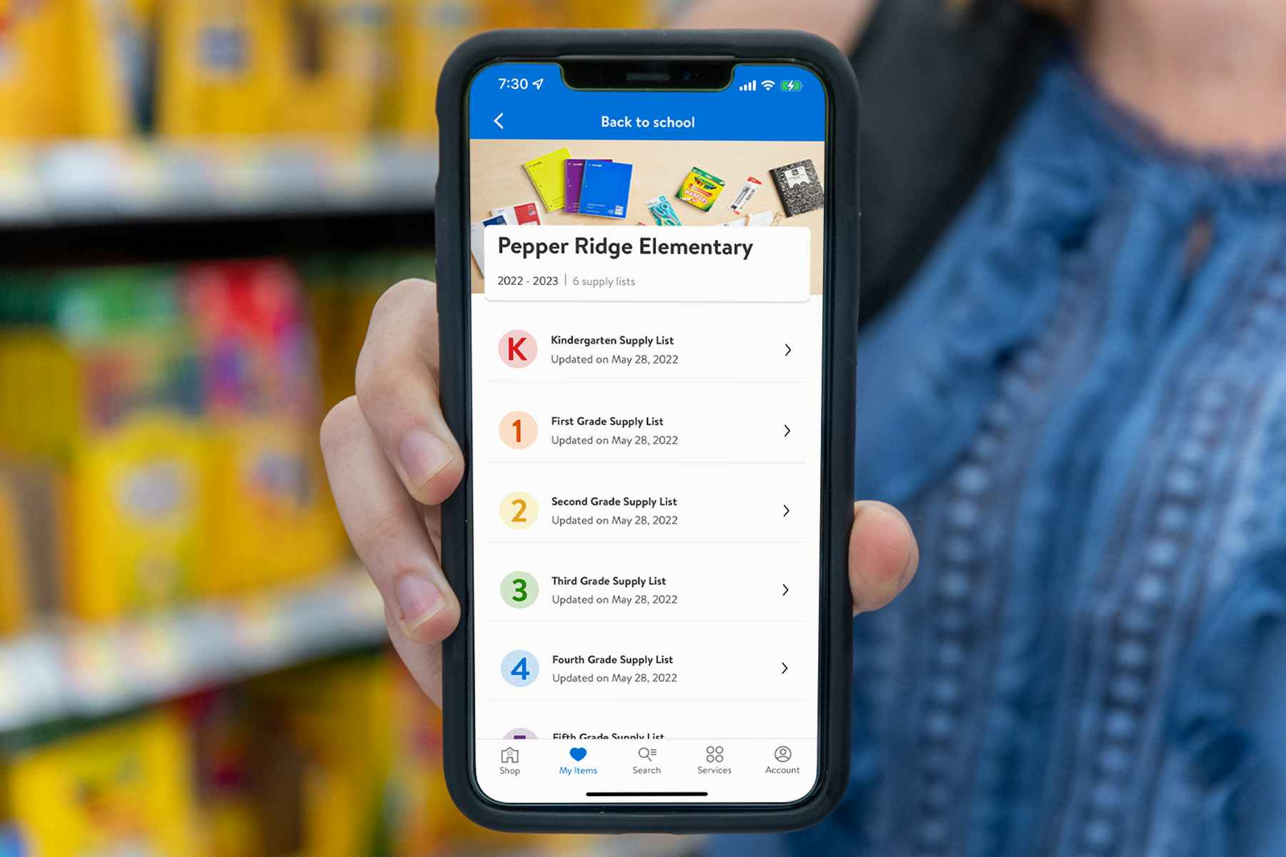 A person holding a cell phone out in front of them. A Walmart school supply list is visible on the screen.