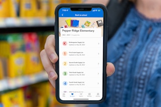 A person holding a cell phone out in front of them. A Walmart school supply list is visible on the screen.