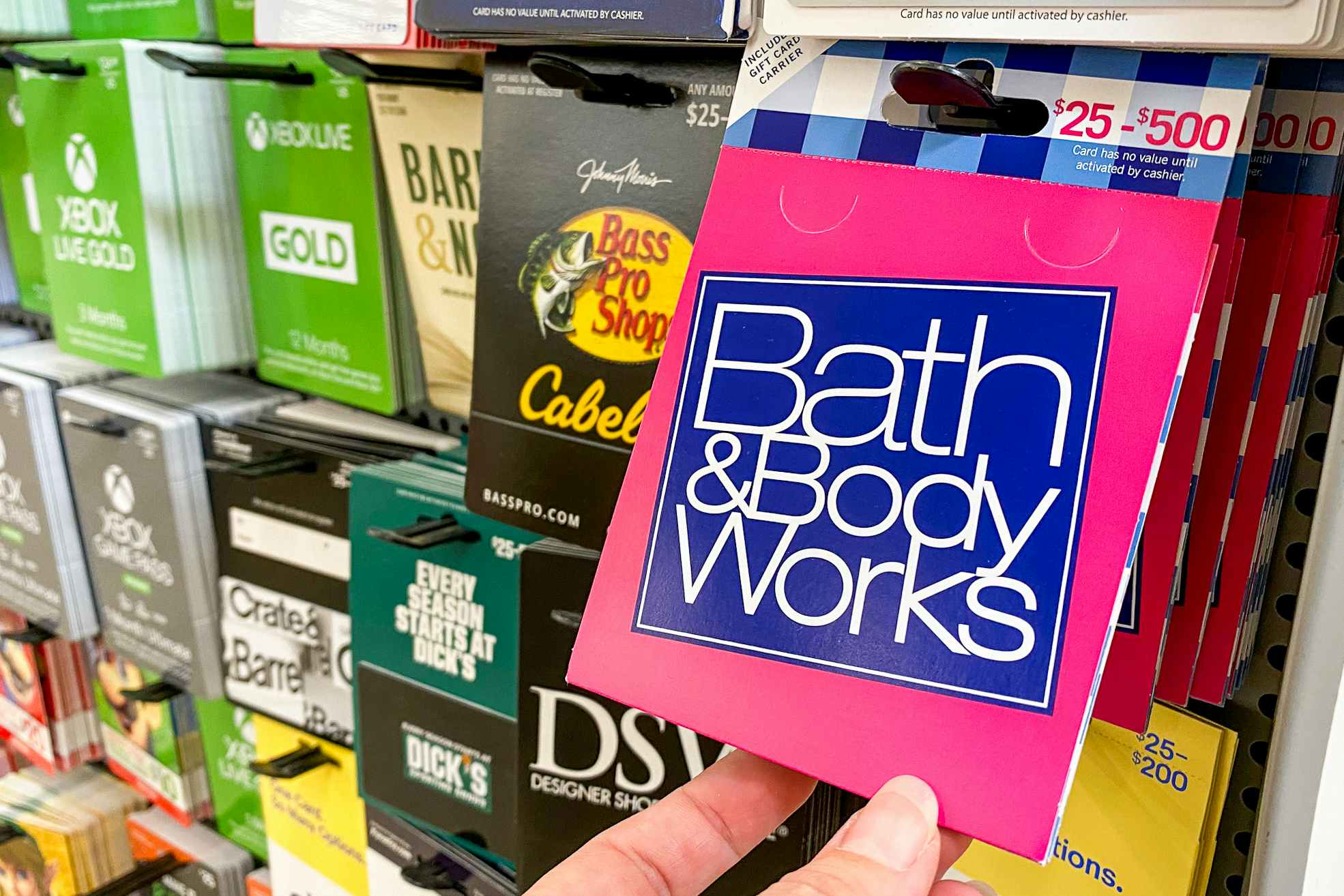 A person's hand taking a Bath & Body Works gift card from a display of gift cards at Walmart.
