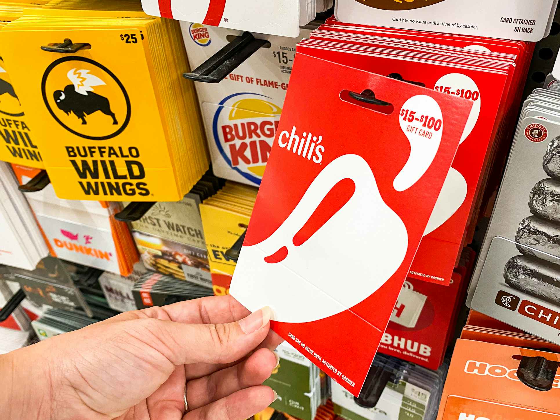 A person's hand taking a Chili's gift card from a display of gift cards at Walmart.