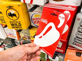 A person's hand taking a Chili's gift card from a display of gift cards at Walmart.