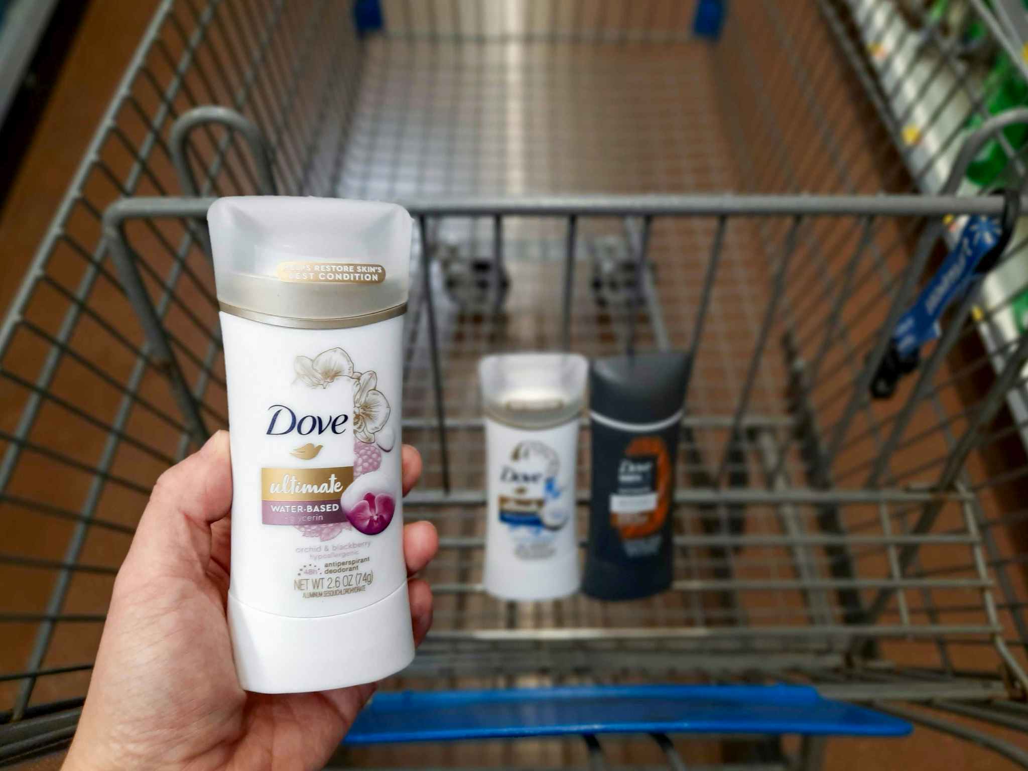 One Dove Ultimate Deodorant product held over Walmart shopping cart. The shopping cart also has two more Dove deodorant products inside it.