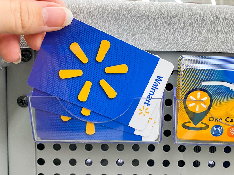 A person's hand taking a Walmart gift card from a display of gift cards at Walmart.