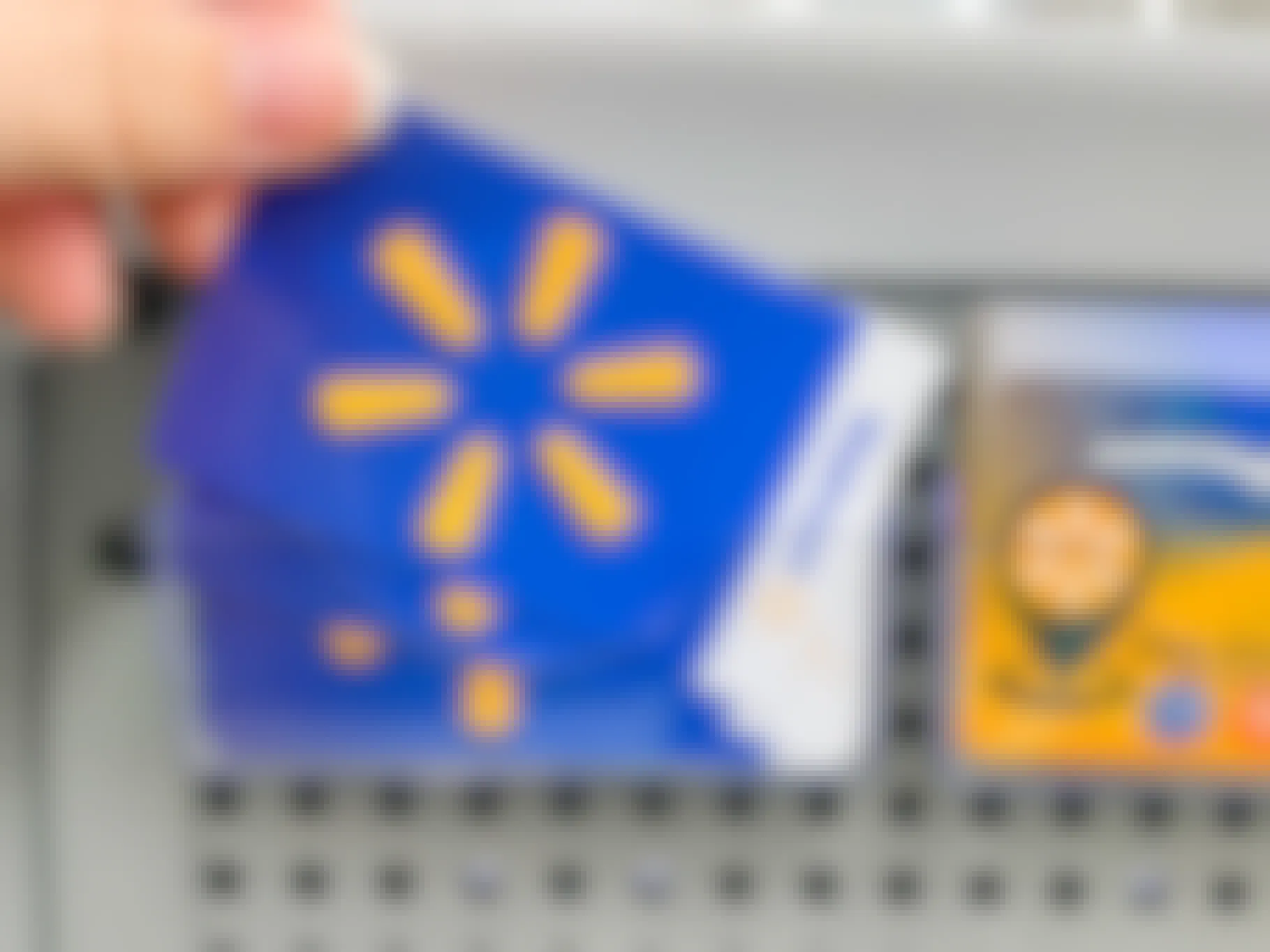 A person's hand taking a Walmart gift card from a display of gift cards at Walmart.