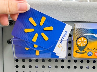 A person's hand taking a Walmart gift card from a display of gift cards at Walmart.