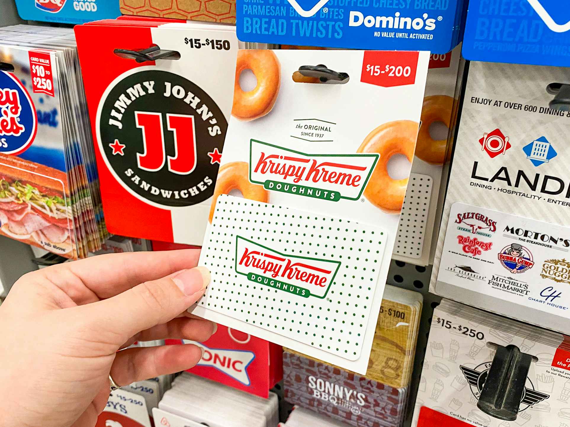 A person's hand taking a Krispy Kreme gift card from a display of gift cards at Walmart.
