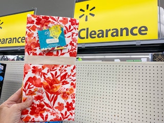 The Pioneer Woman Kitchen Towels held in front of clearance sign at Walmart. Clearance sticker reads $3, regularly $5.94.