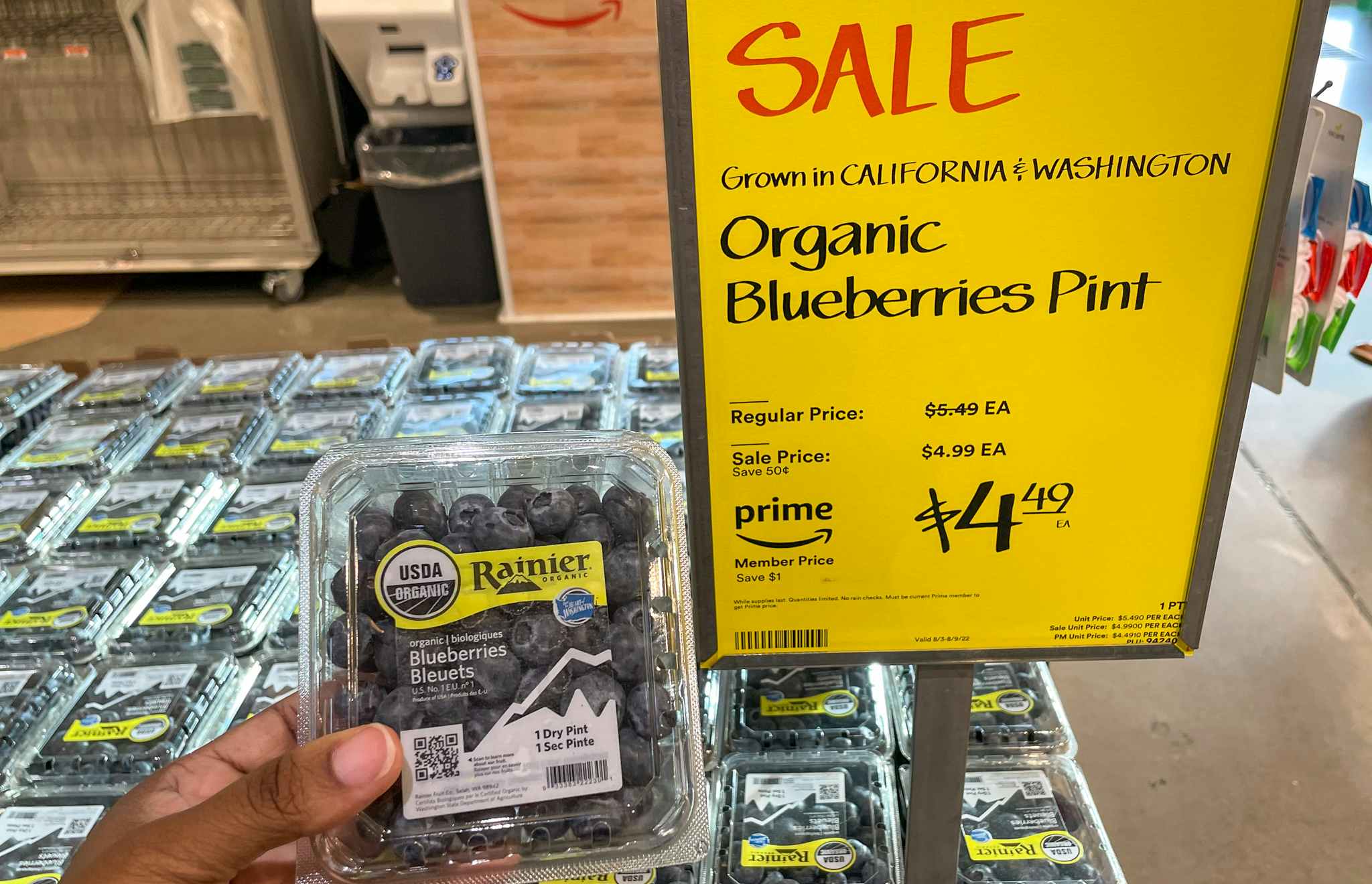 package of blueberries held in hand near sales sign at whole foods