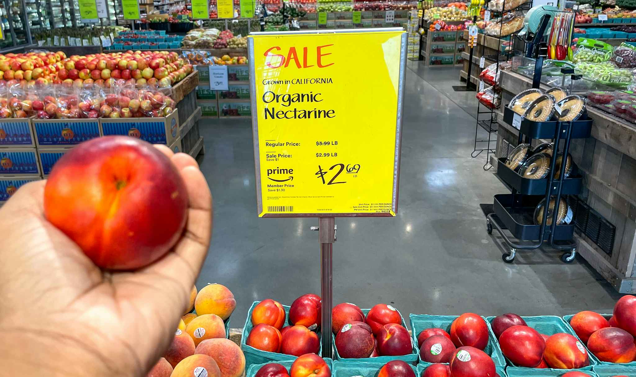 organic nectarine held in hand near sales sign at whole foods