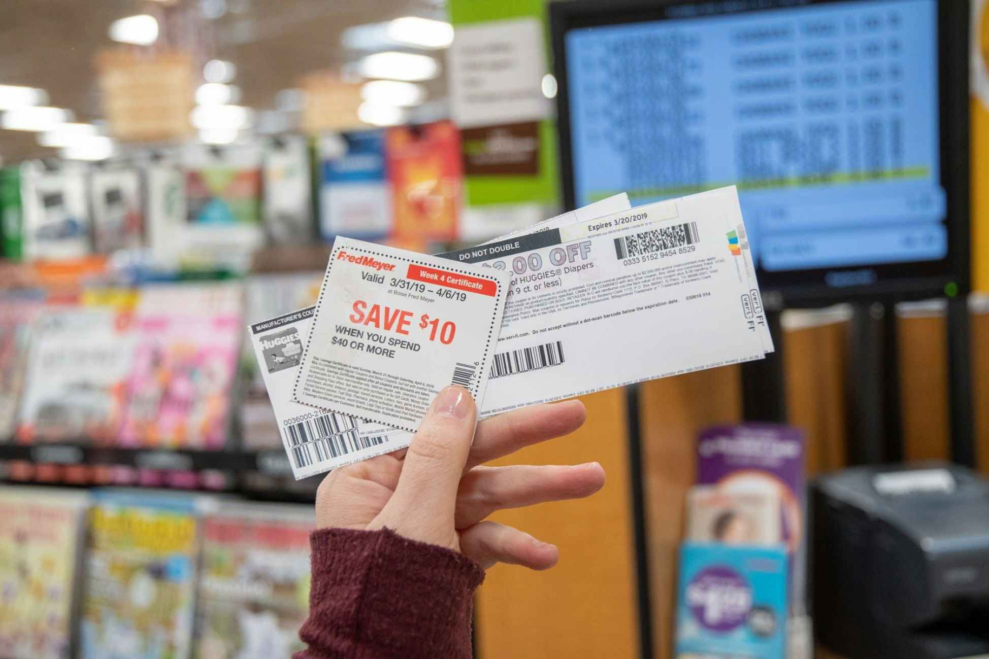 hand holding coupons near self-checkout lane in store