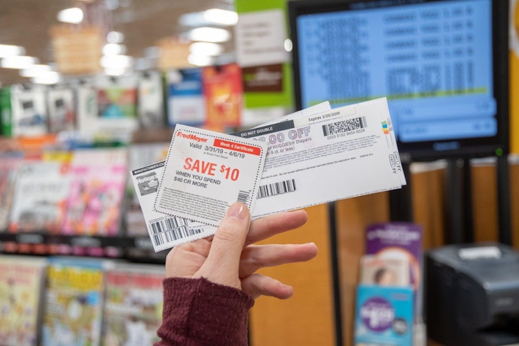 hand holding coupons near self-checkout lane in store