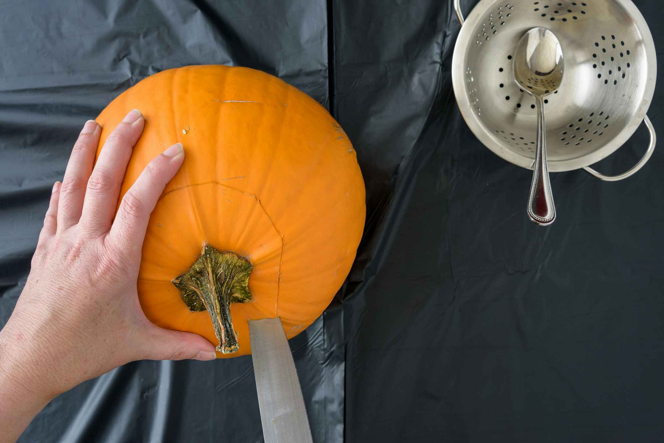 woman cutting off top of pumpkin with knife