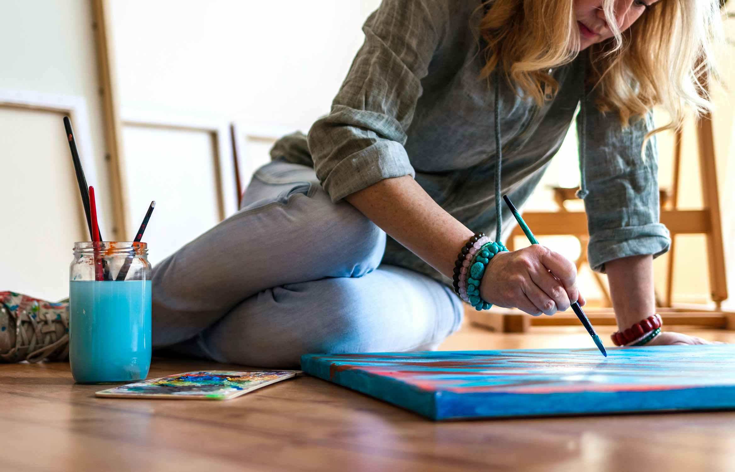 woman sitting on floor painting abstract on canvas