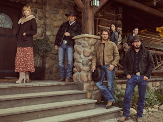 Cast members of Yellowstone posed around a front porch of a farmhouse.