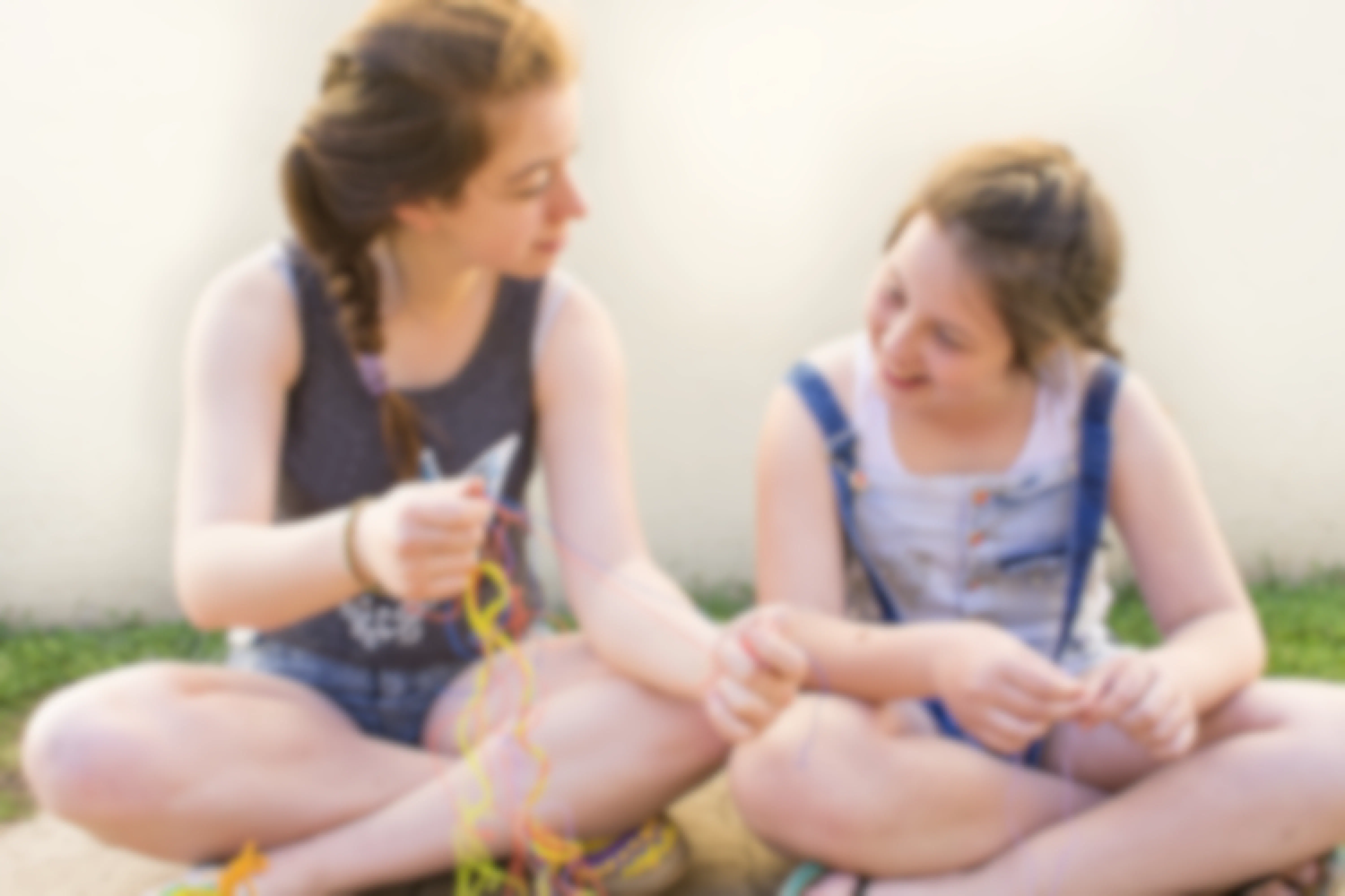 Two young girls sitting outside and working on making friendship bracelets with embroidery floss.