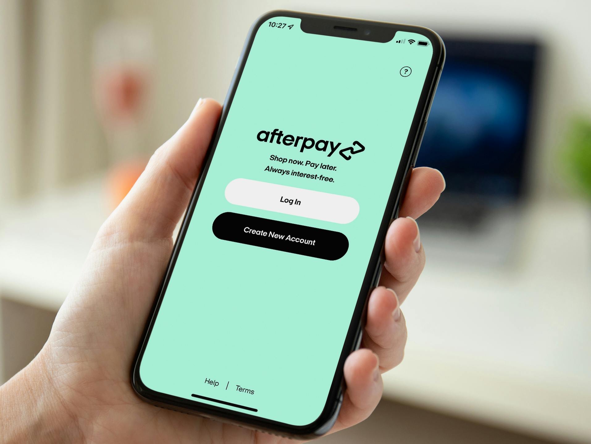 A person's hand holding up a cell phone displaying the Afterpay app's login screen.