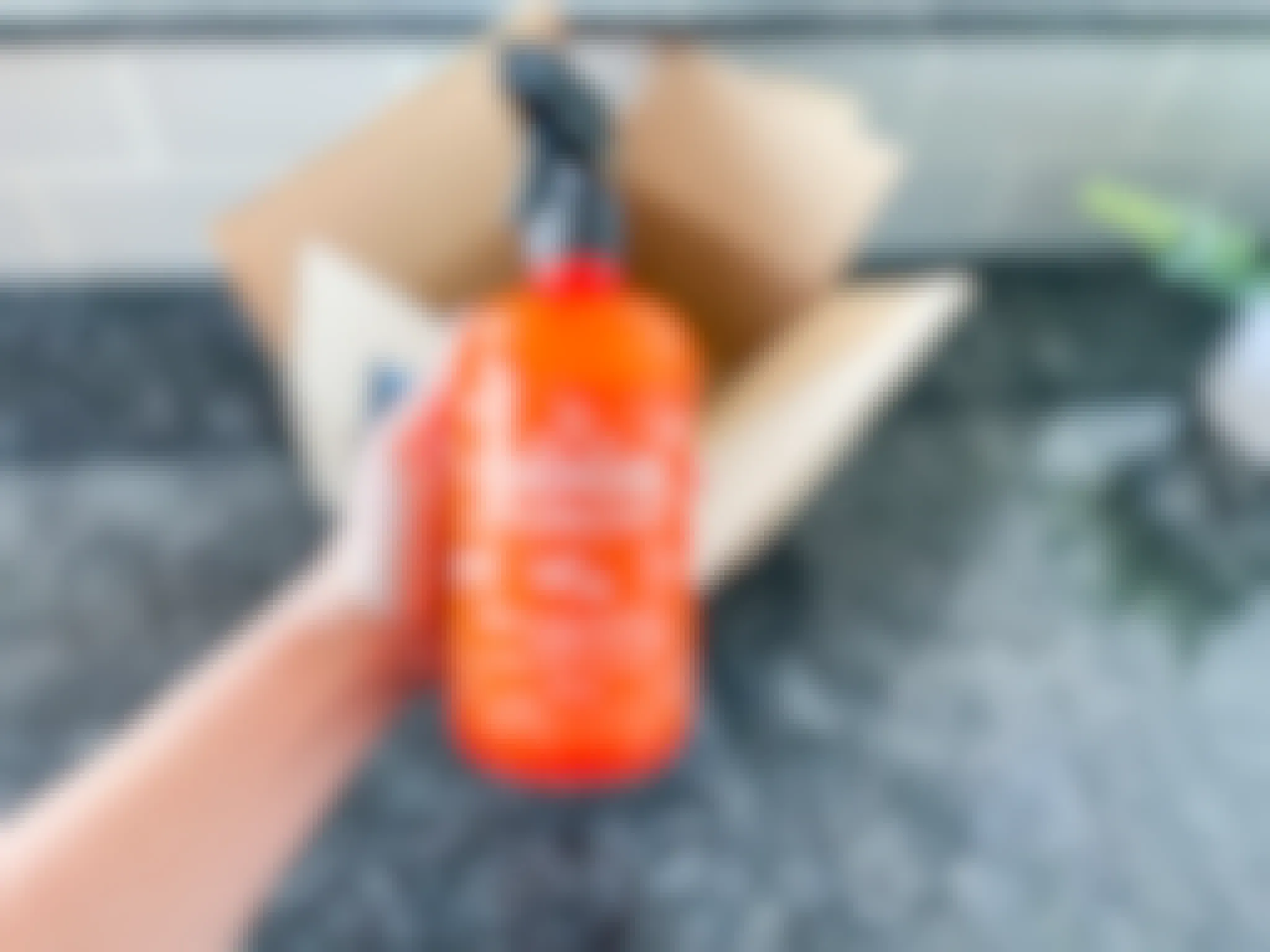 A hand holding an Angry Orange spray in front of an open delivery box.