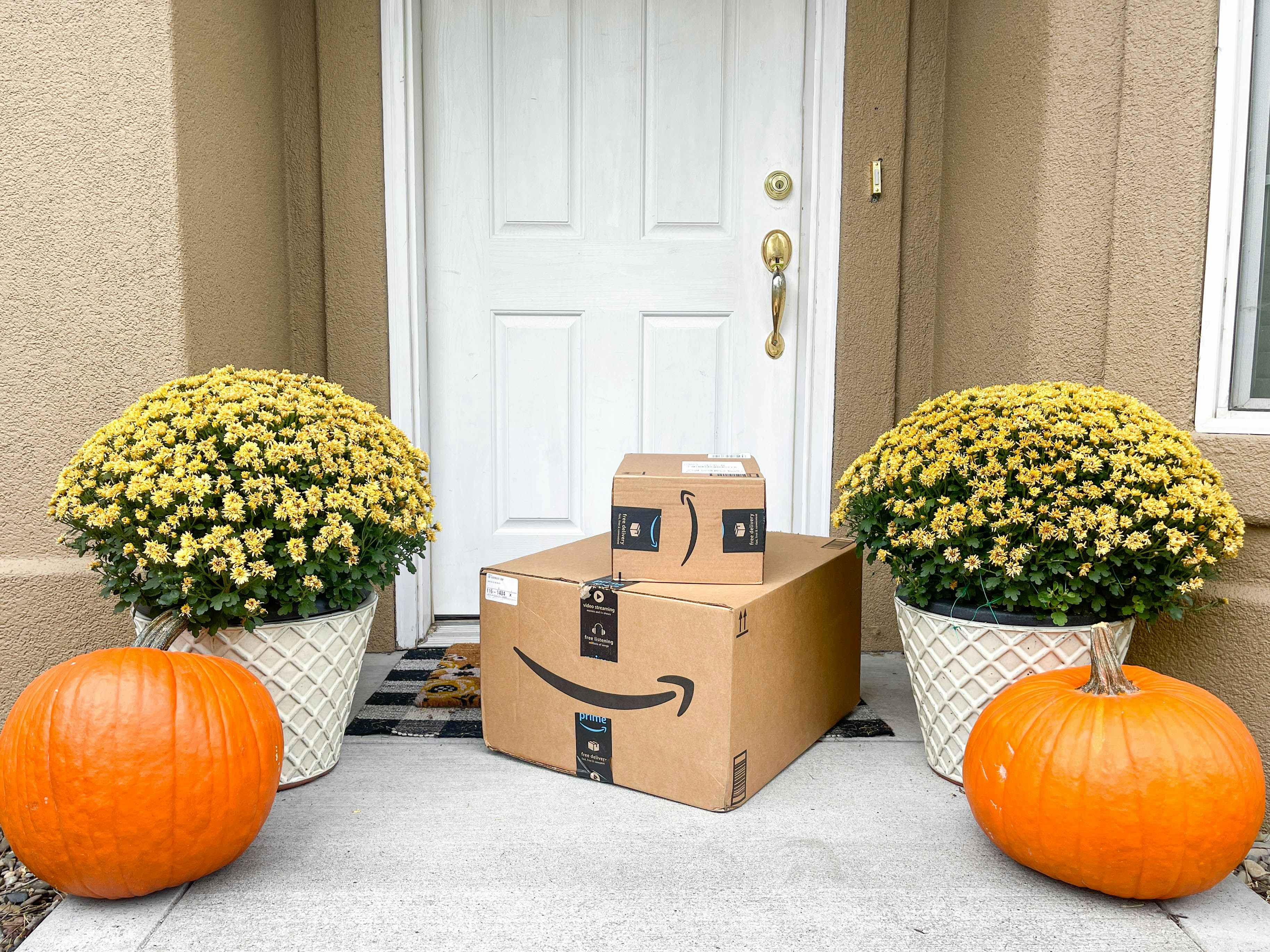 Amazon boxes on a doorstep with fall mums and pumpkins on each side