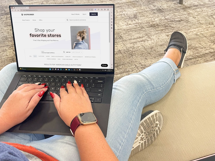 person with a laptop sitting on couch with american eagle page on shop runner website
