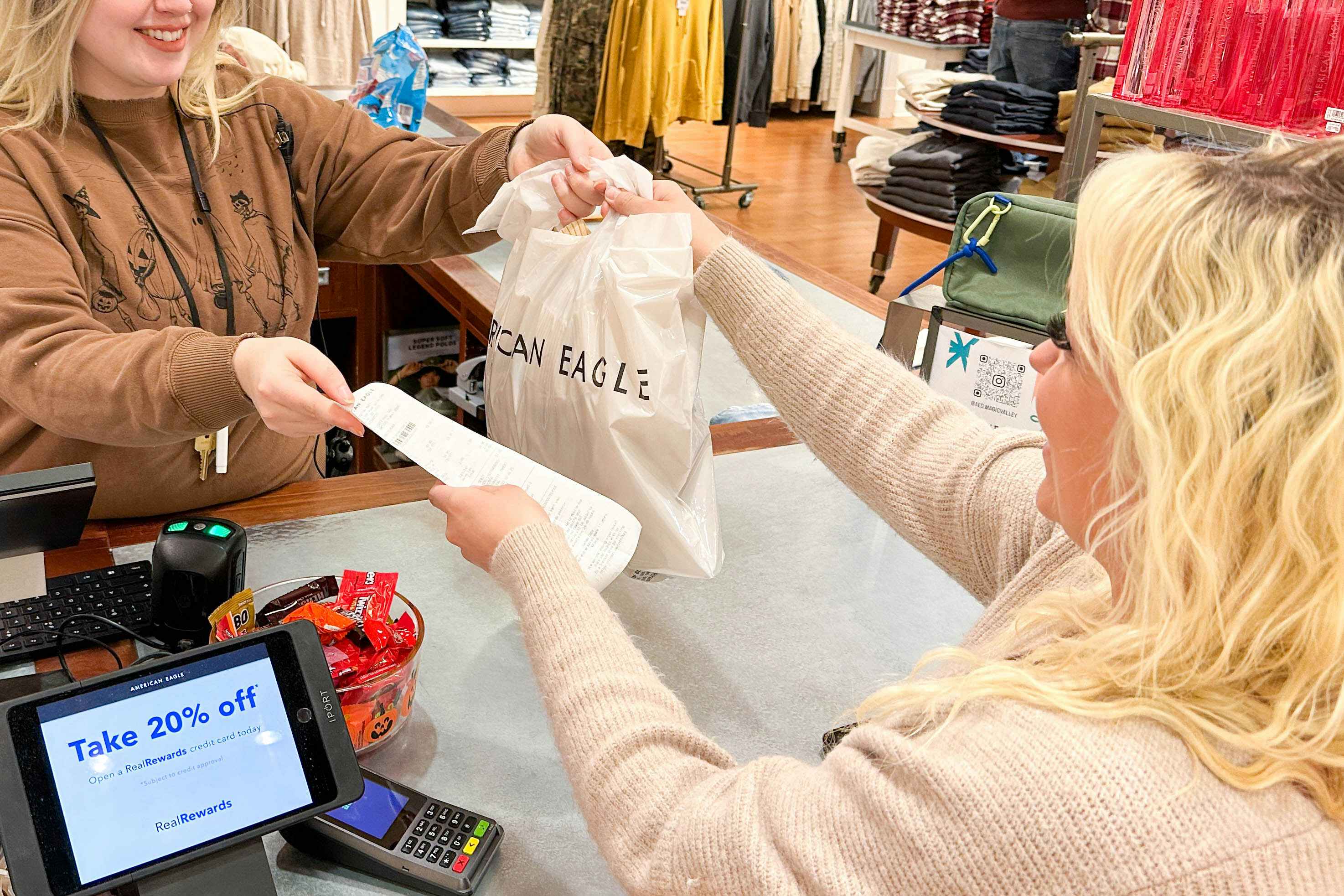 a woman grabbing her bag and reciept from an employee in american eagle 