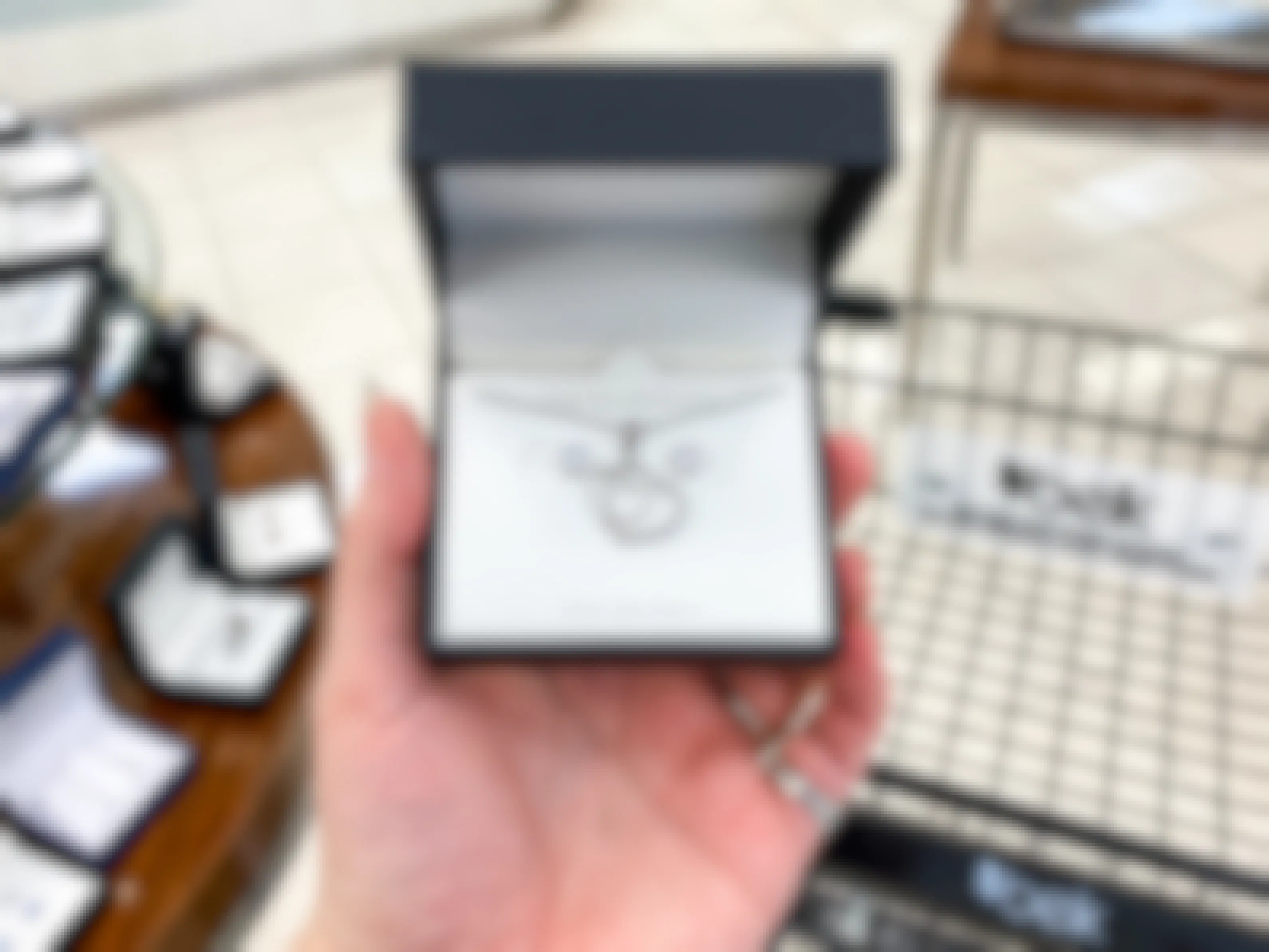 A person's hand holding a jewelry set box in front of a shelf and cart at Belk.