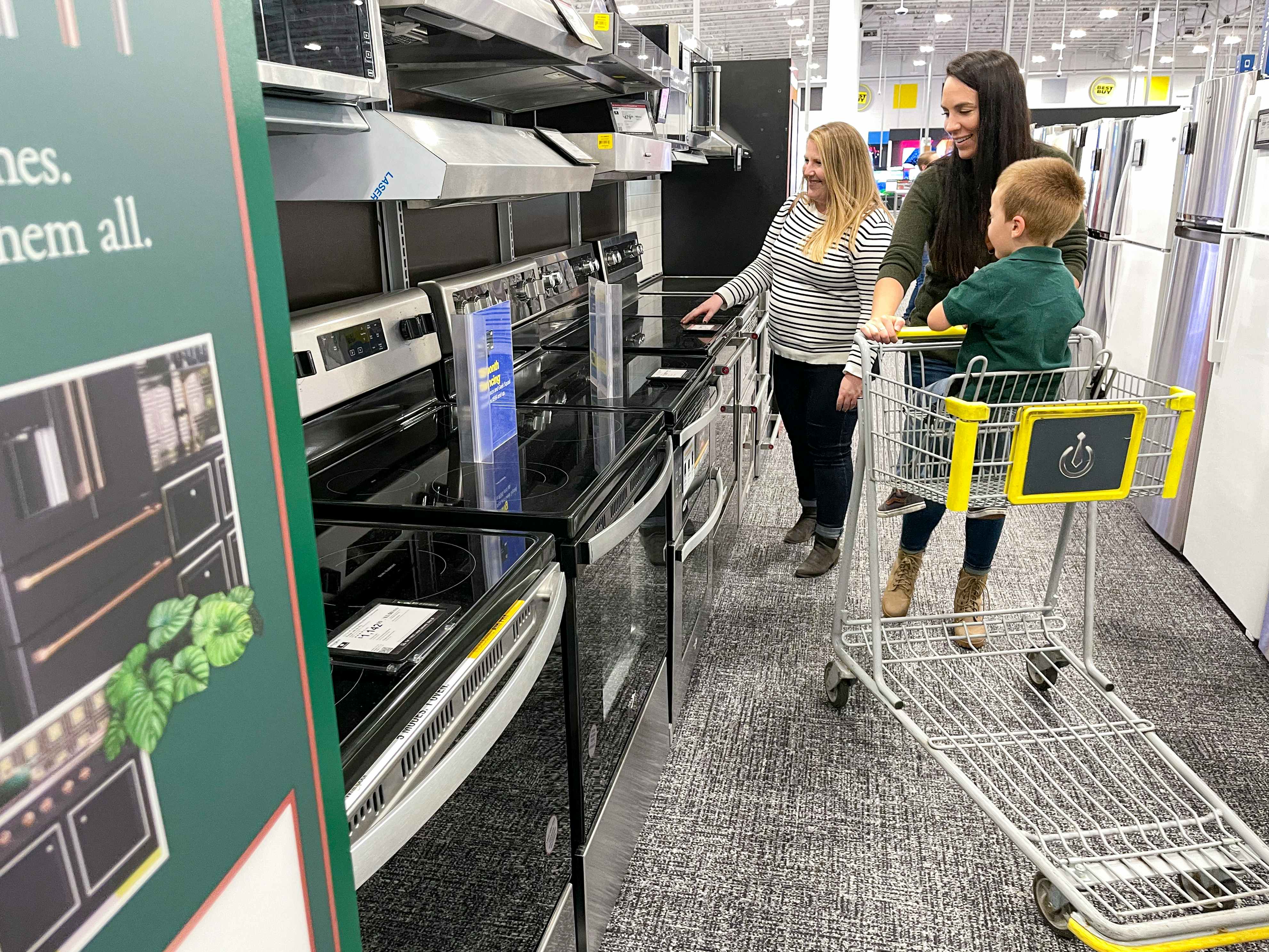 A group of people shopping in the appliance section at best buy.