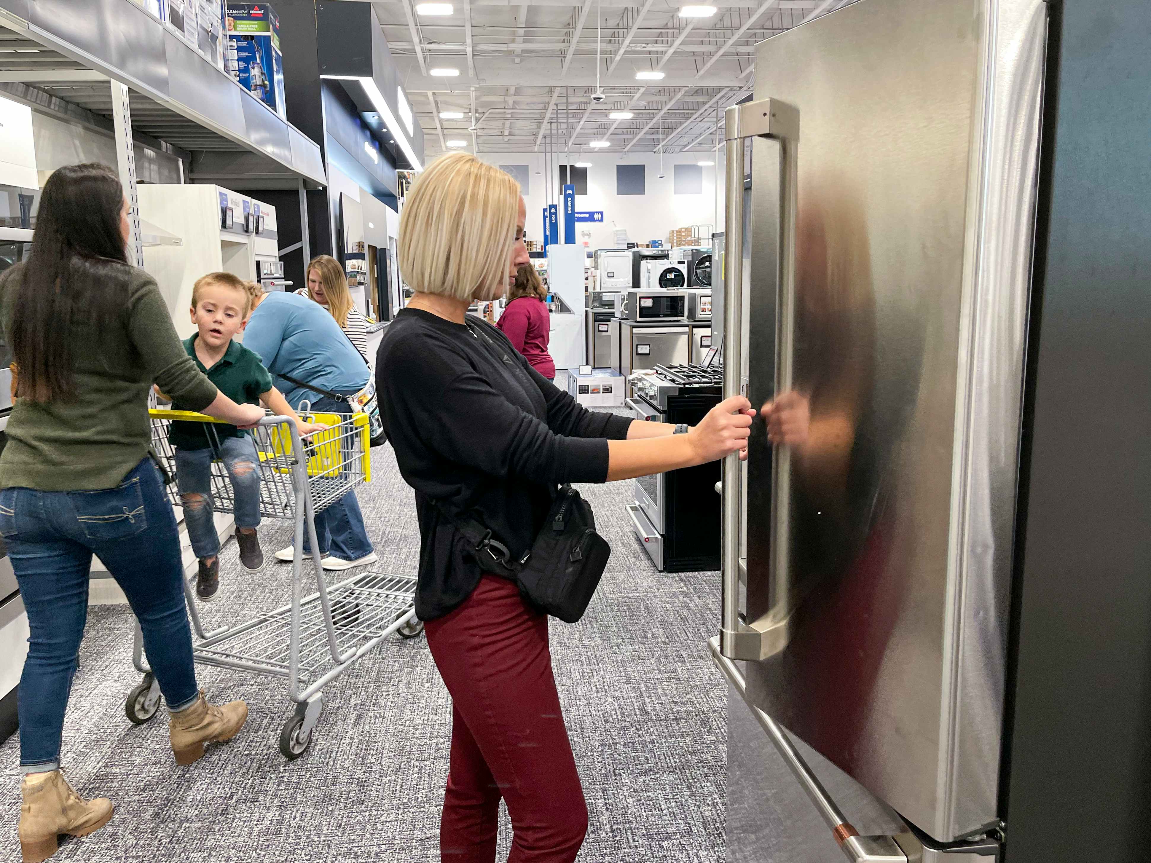 A group of people shopping in the appliance section at best buy.