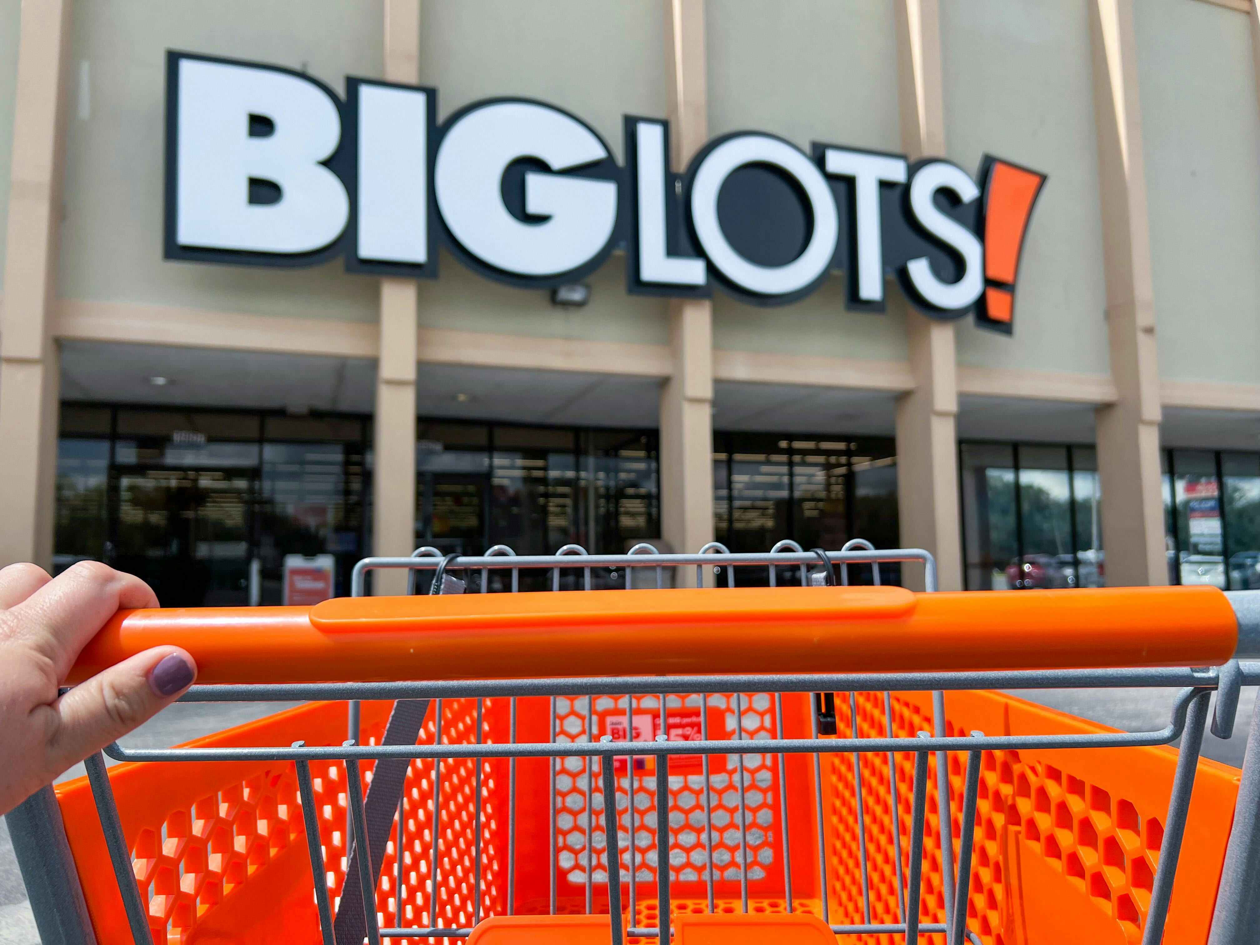 Hand pushing an orange Big Lots shopping cart into the store