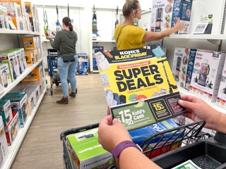 People shopping in the appliance section of Kohl's, one person holding a Black Friday ad.