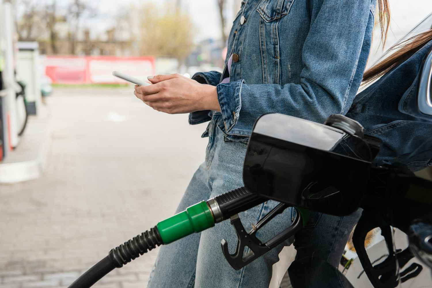 woman looking at phone while filling up car with gas