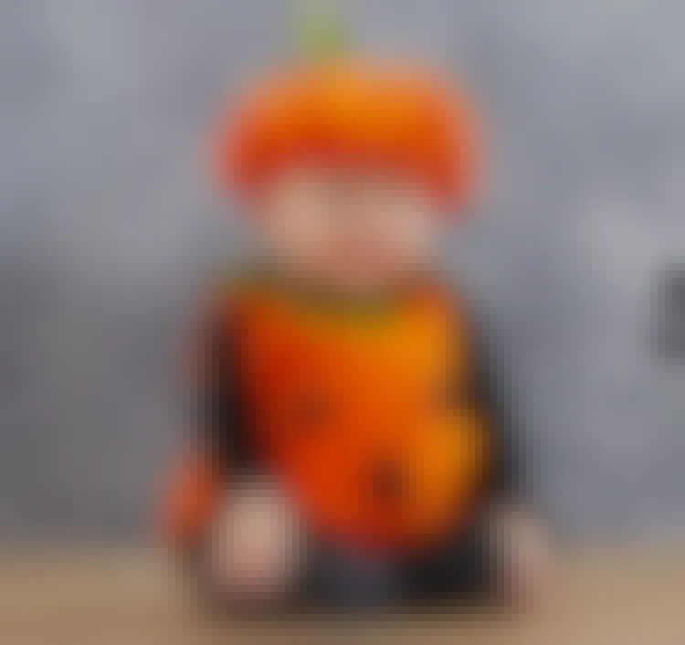 A baby sitting on a wood floor wearing a pumpkin outfit.