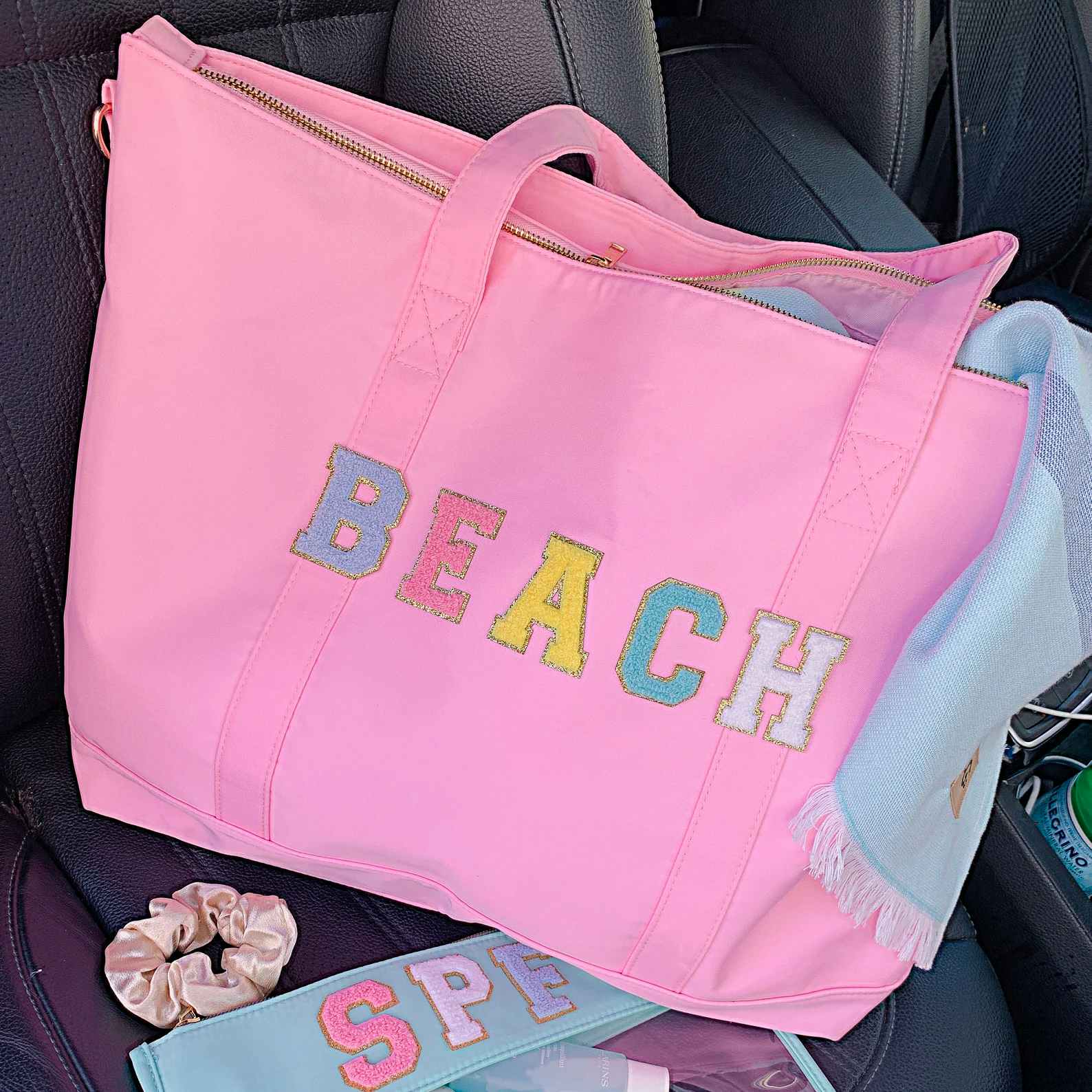 A tote bag that says "Beach" on the front in custom patches sitting in the passenger seat of a vehicle.