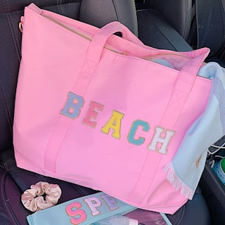 A tote bag that says "Beach" on the front in custom patches sitting in the passenger seat of a vehicle.