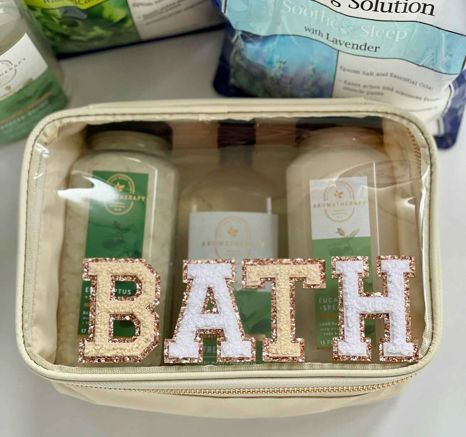 A custom clear-front pouch with the word "bath" in patches, sitting on a bathroom counter next to some bath supplies.