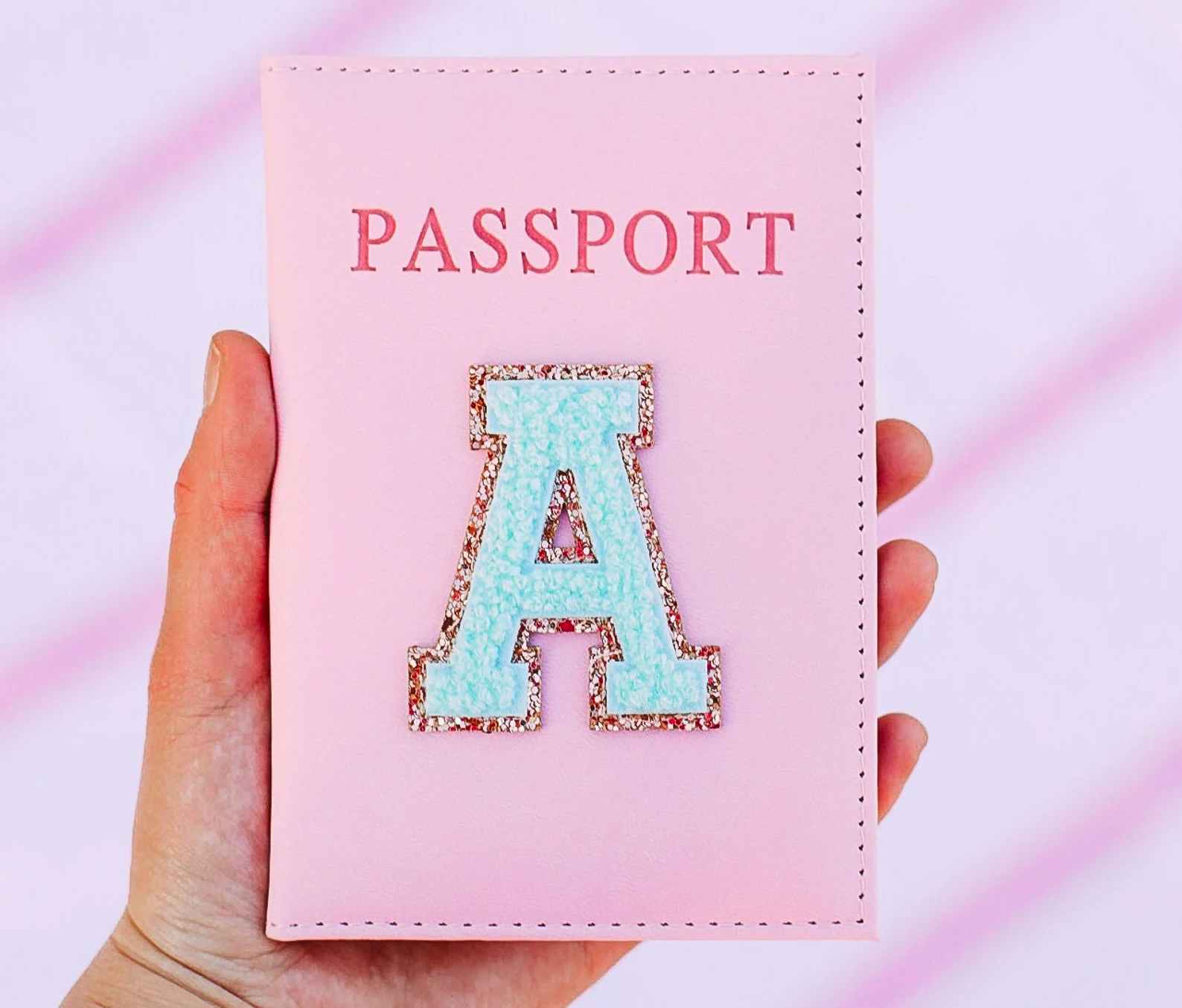 A person's hand holding up a customized passport cover with the varsity letter A on it.